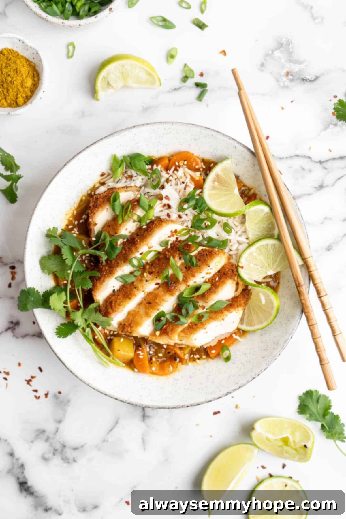 Bowl of vegan katsu curry garnished with cilantro and lime, with chopsticks on top