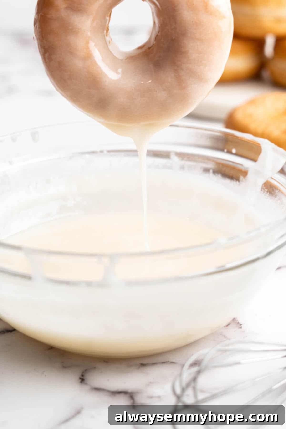 Dipping a warm vegan donut into a bowl of sweet glaze