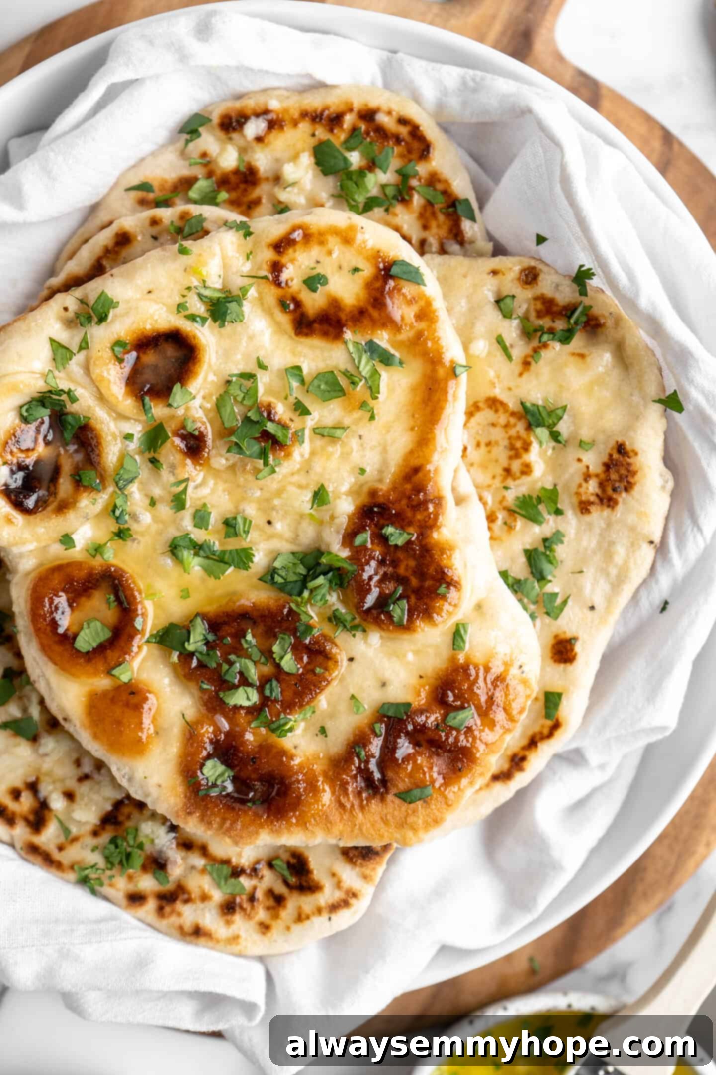 This vegan garlic naan recipe is chewy, soft, and easy to make at home! It's full of garlic flavour and perfect for pairing with curry! Freshly cooked vegan garlic naan stacked high in a towel-lined bowl, ready to be served or stored.