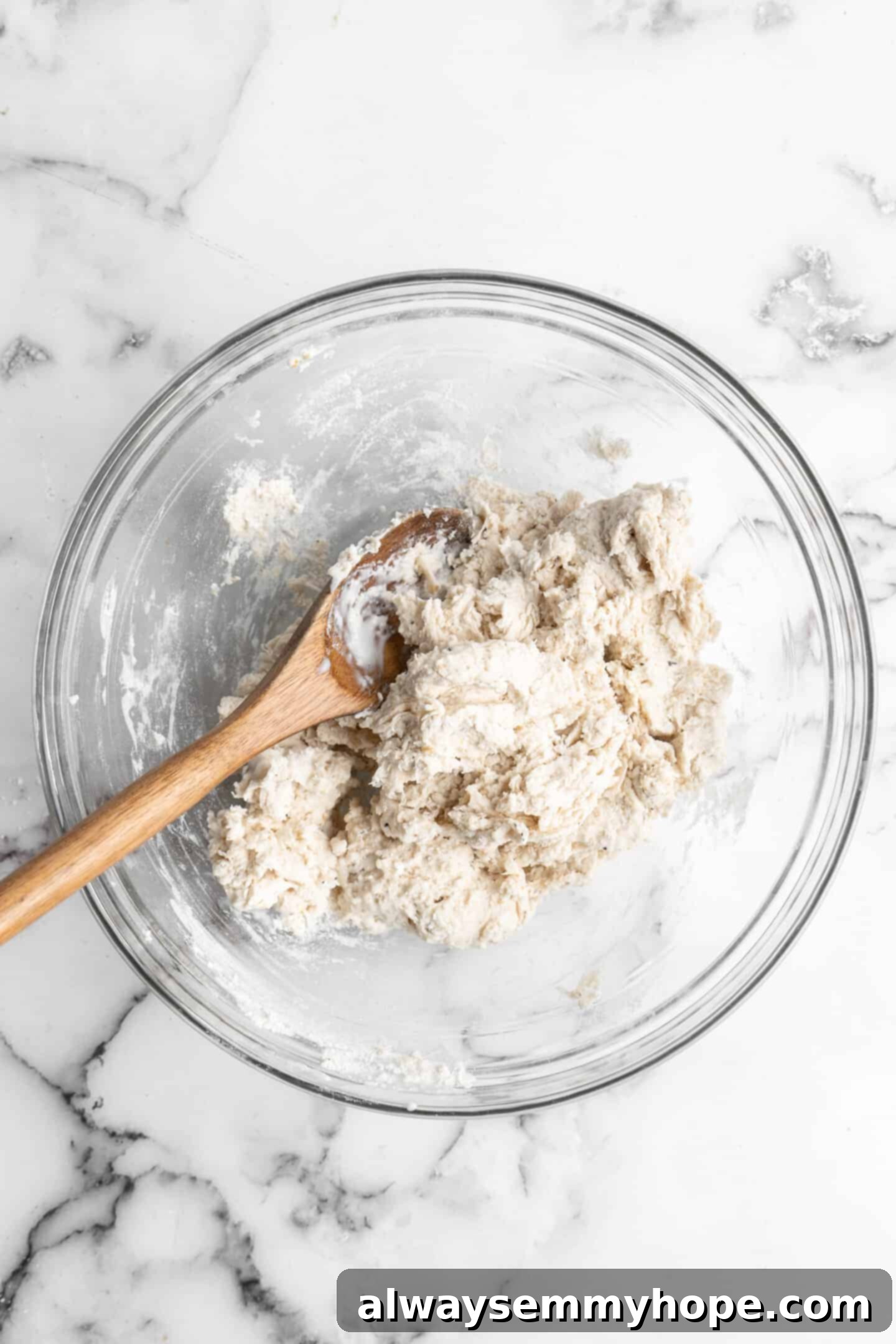 This vegan garlic naan recipe is chewy, soft, and easy to make at home! It's full of garlic flavour and perfect for pairing with curry! Overhead view of garlic naan dough being mixed in a glass bowl, forming a shaggy texture.