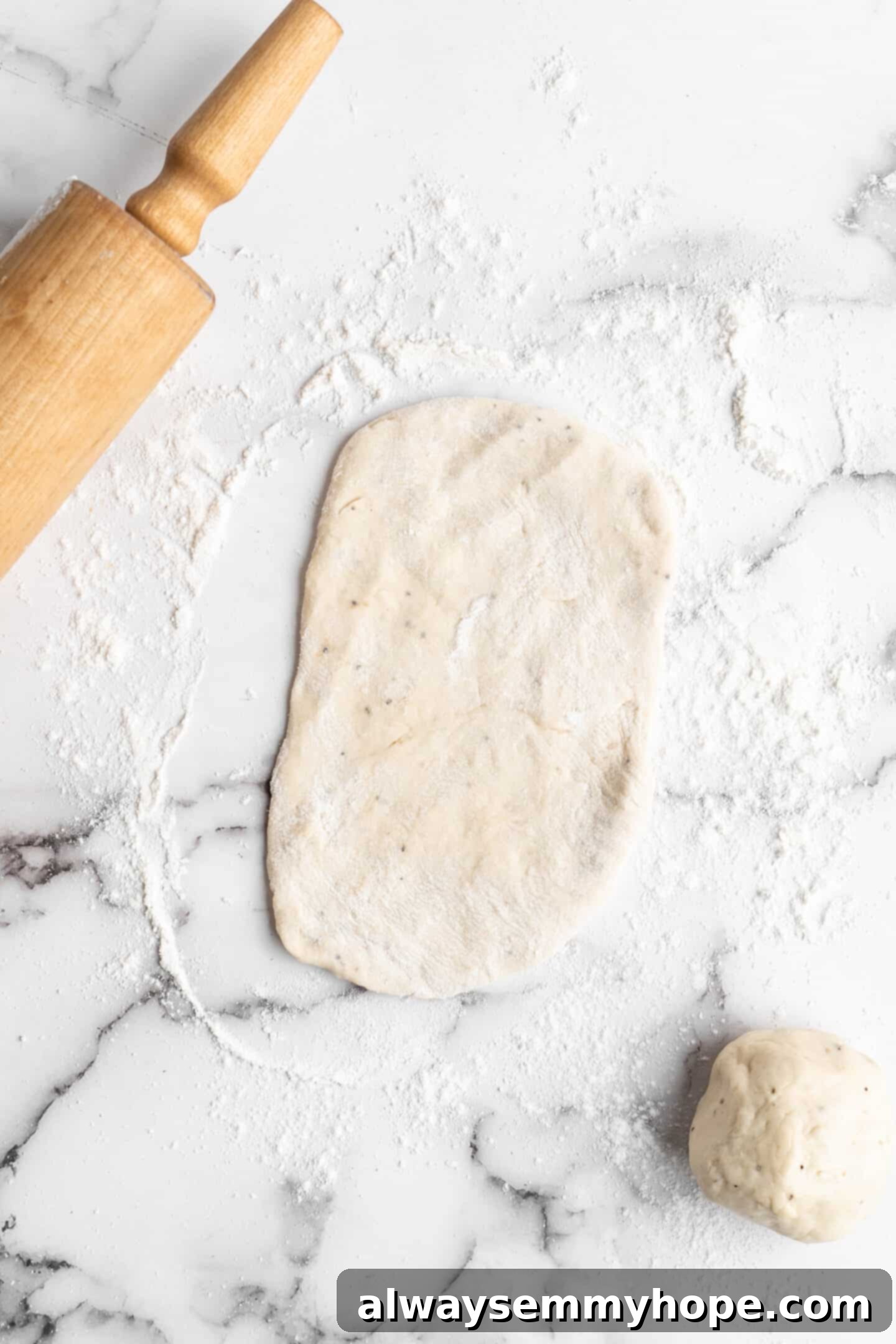 This vegan garlic naan recipe is chewy, soft, and easy to make at home! It's full of garlic flavour and perfect for pairing with curry! Overhead view of a rolled-out naan on a floured surface, ready for cooking.