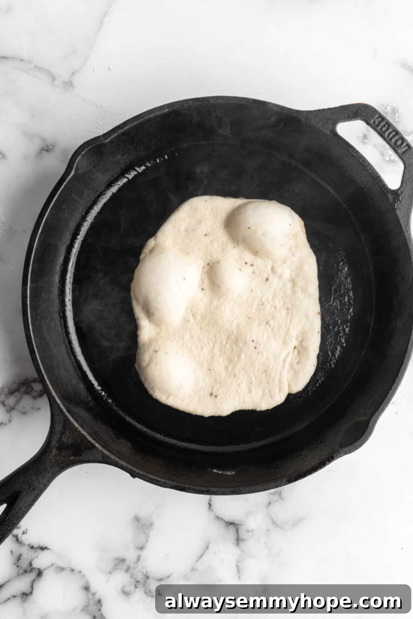 This vegan garlic naan recipe is chewy, soft, and easy to make at home! It's full of garlic flavour and perfect for pairing with curry! Overhead view of naan cooking in a hot cast iron skillet, showing the beginning of bubbles.