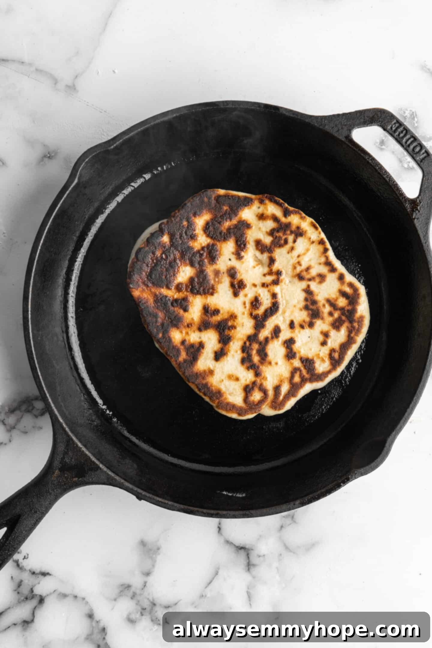 This vegan garlic naan recipe is chewy, soft, and easy to make at home! It's full of garlic flavour and perfect for pairing with curry! A piece of vegan naan bread cooking in a cast iron skillet, showing a nicely browned surface.