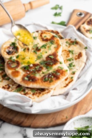 This vegan garlic naan recipe is chewy, soft, and easy to make at home! It's full of garlic flavour and perfect for pairing with curry! Drizzling garlic butter over freshly cooked homemade garlic naan.