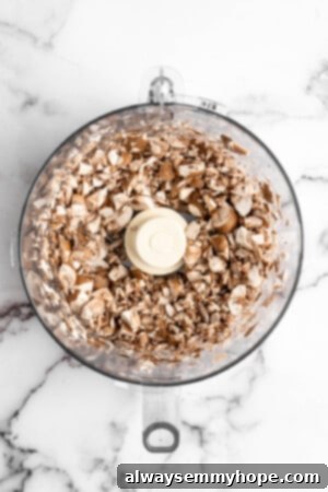 Cremini mushrooms being pulsed in a food processor, creating a coarse, ground-like texture.