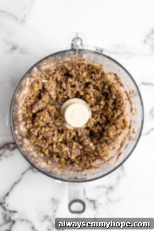 The blended mixture of coarsely chopped lentils and mushrooms in a food processor, resembling ground plant-based 'meat'.