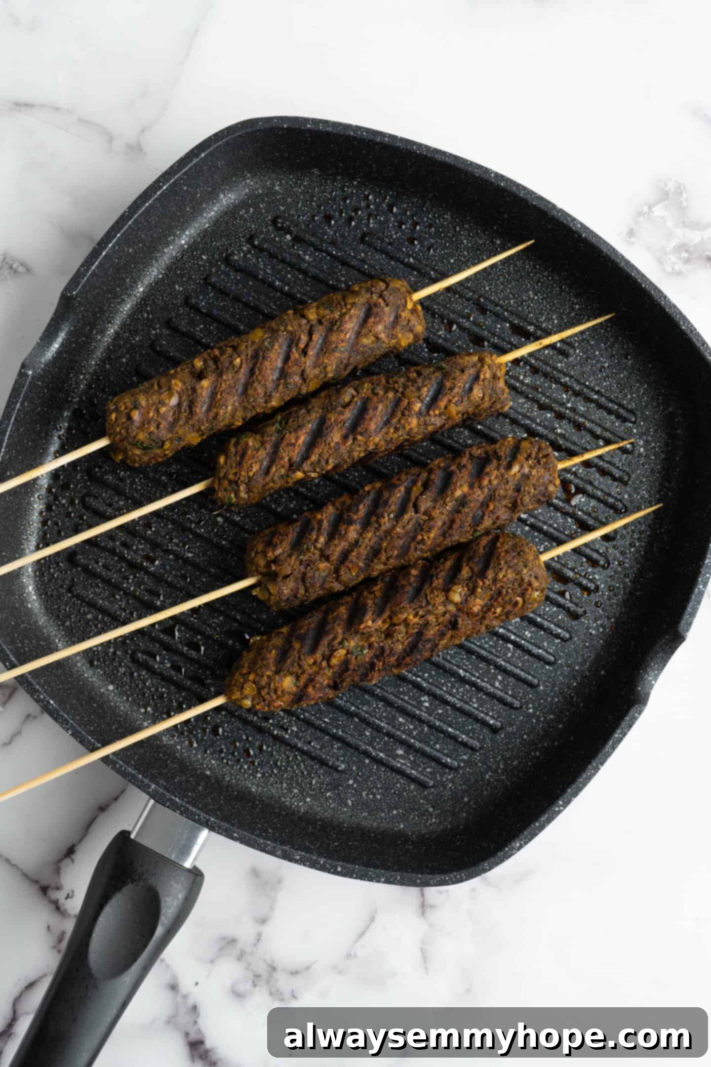 Vegan kofta skewers grilling on a ribbed grill pan, showing clear grill marks and beginning to char.