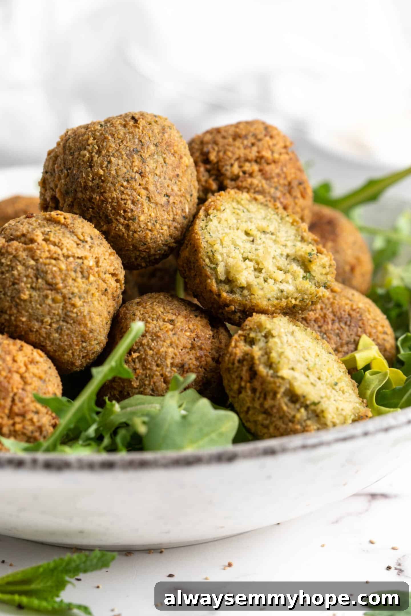 This homemade falafel recipe is just like the kind they make at restaurants. Fluffy on the inside, crispy on the outside, and so delicious! Closeup of falafel in bowl with greens, with one cut open to show fluffy inside