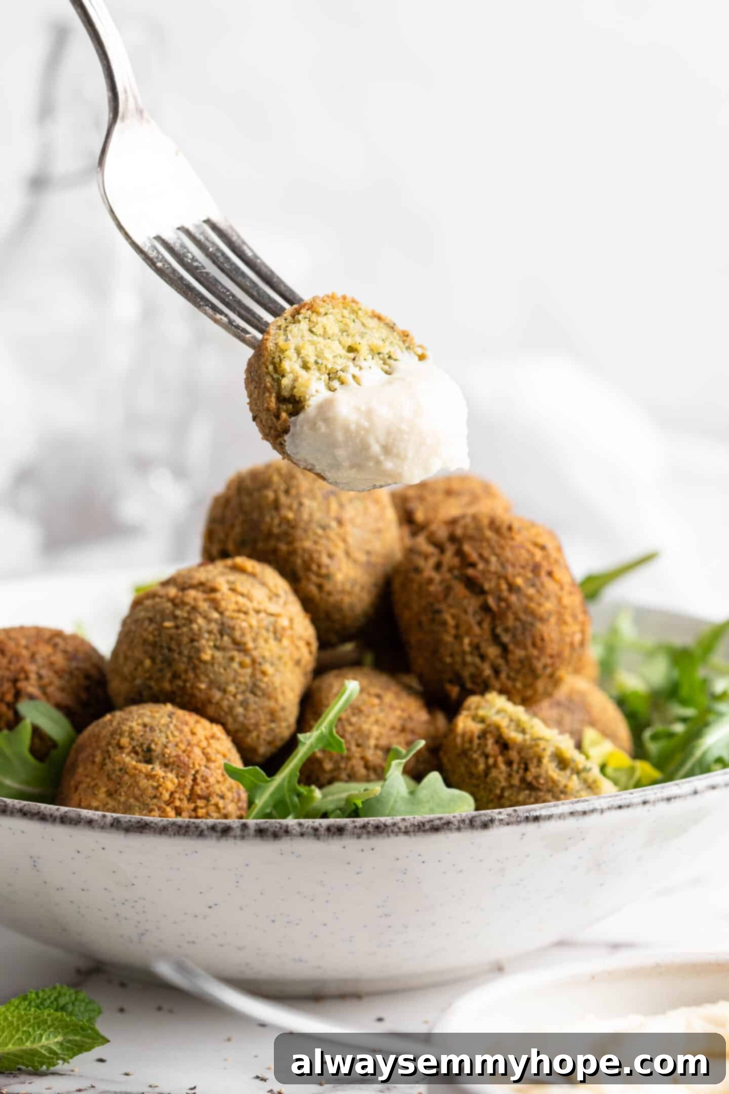 This homemade falafel recipe is just like the kind they make at restaurants. Fluffy on the inside, crispy on the outside, and so delicious! Falafel on a fork with tahini sauce