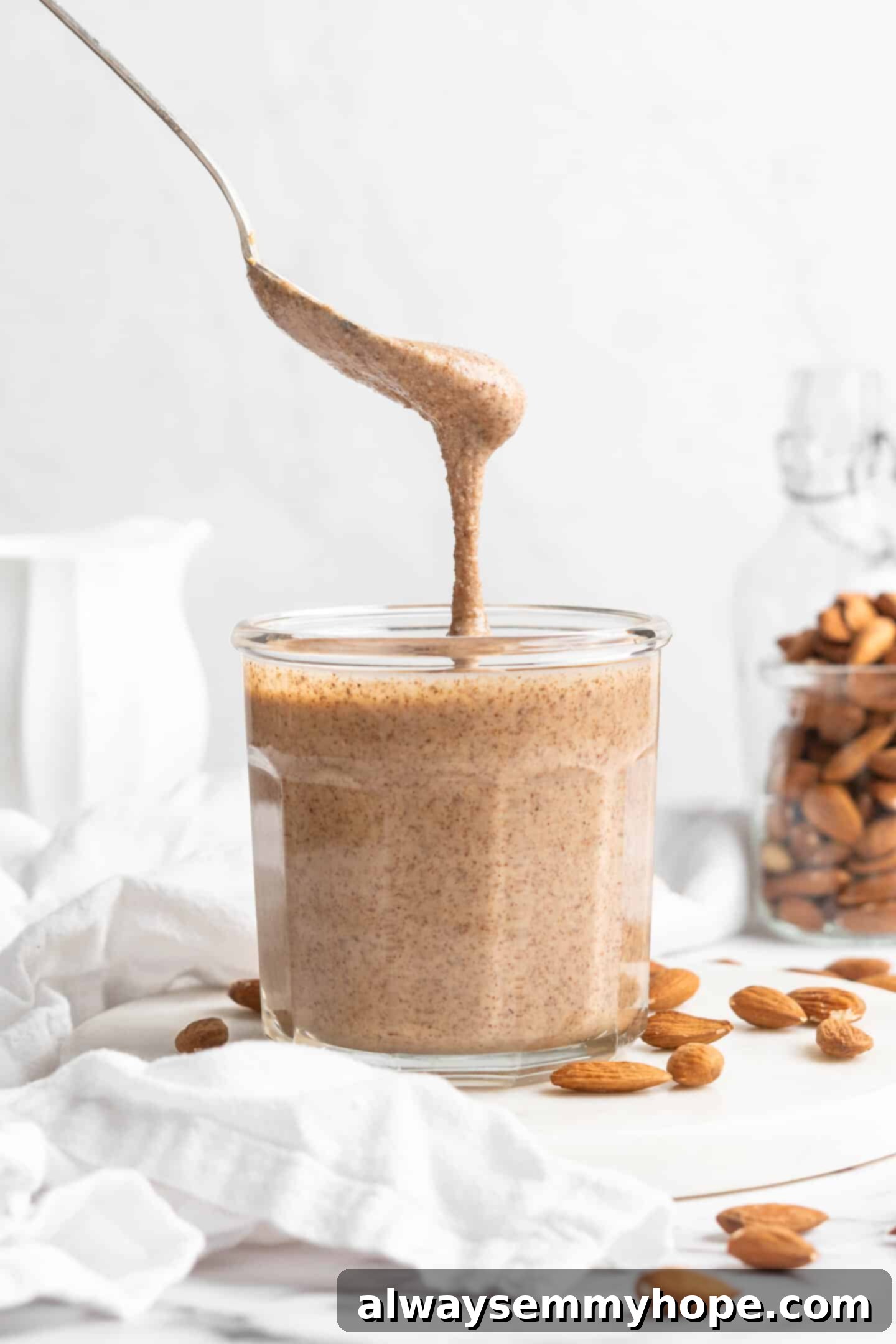 Spoon drizzling fresh homemade almond butter into a glass jar