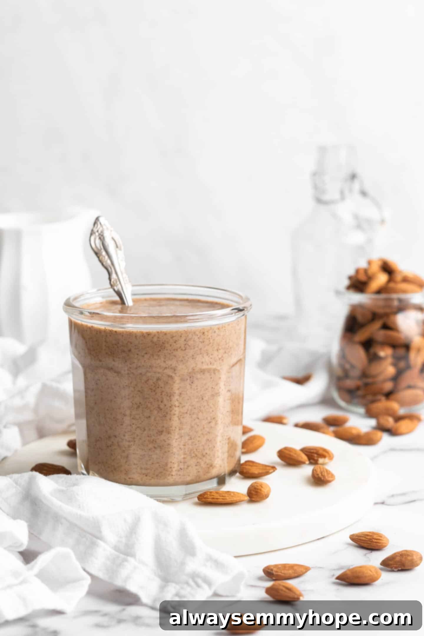 Glass jar filled with homemade almond butter, with whole almonds scattered in the background