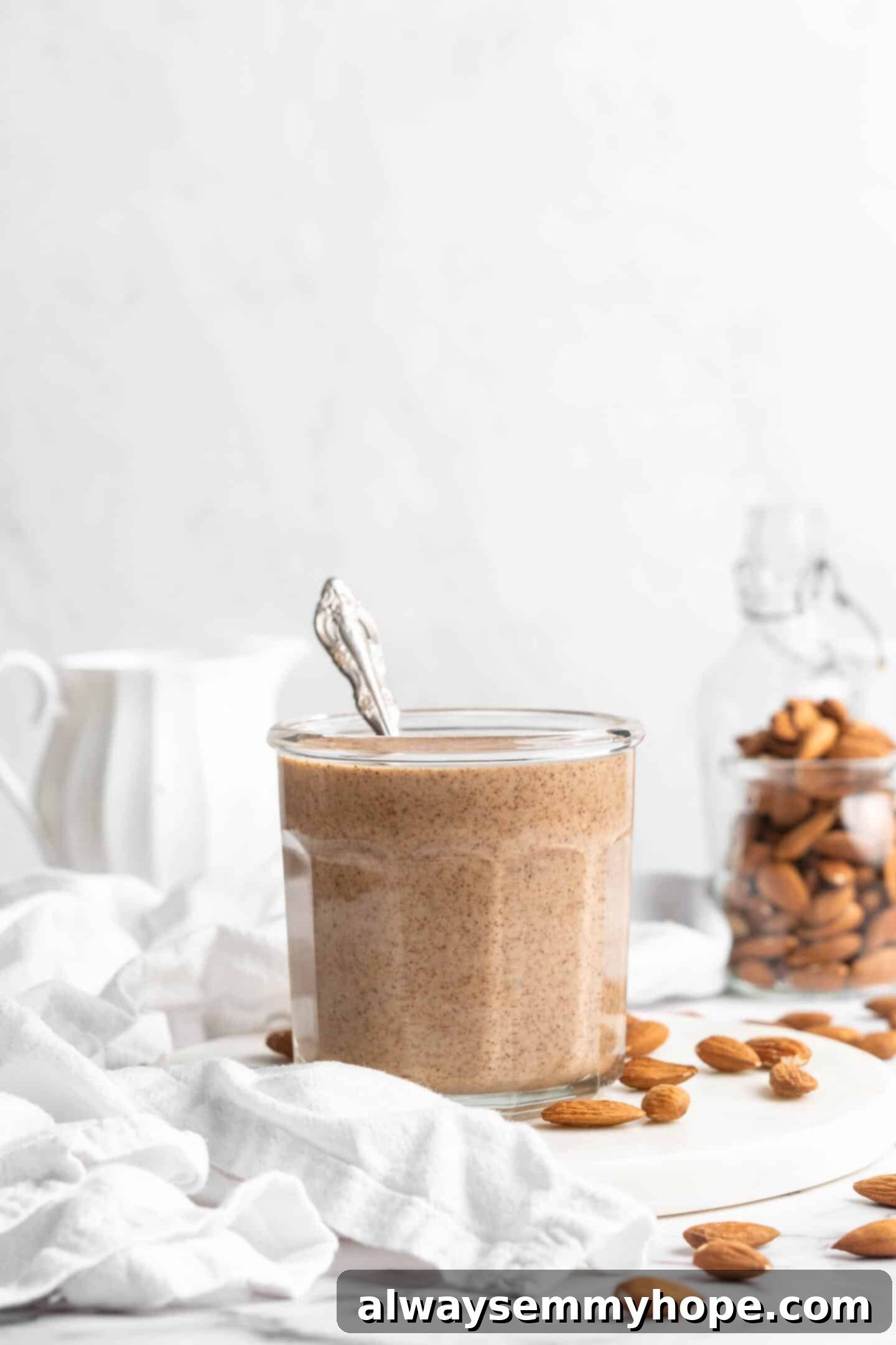 Glass jar of homemade almond butter with a spoon inside, ready to be enjoyed