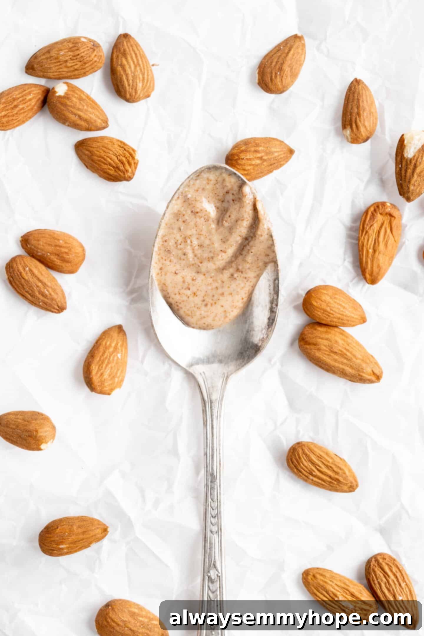 Spoon with almond butter, surrounded by whole almonds on a wooden surface