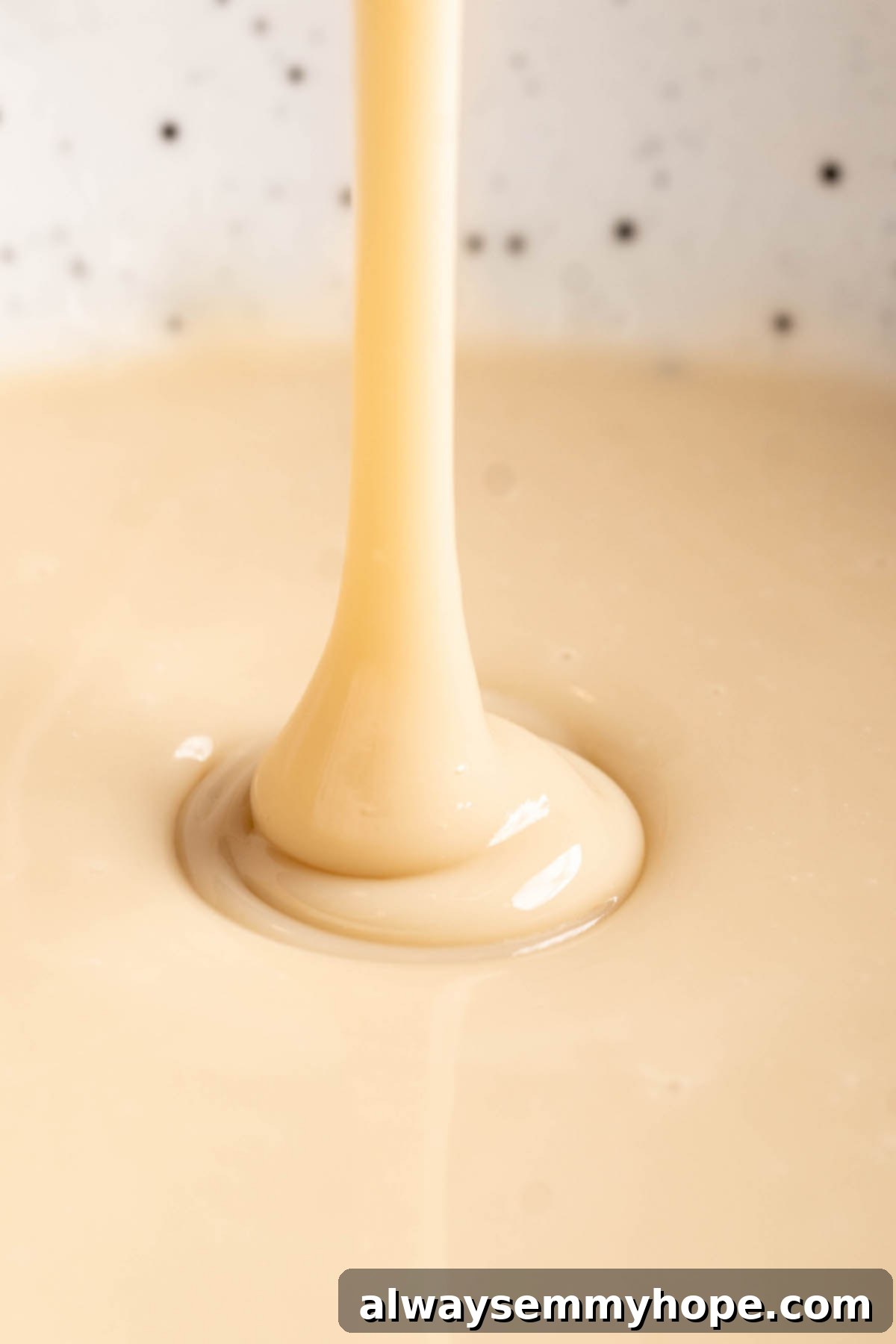 Close-up view of thick vegan condensed milk being poured from a spoon into a bowl, highlighting its rich, syrupy consistency