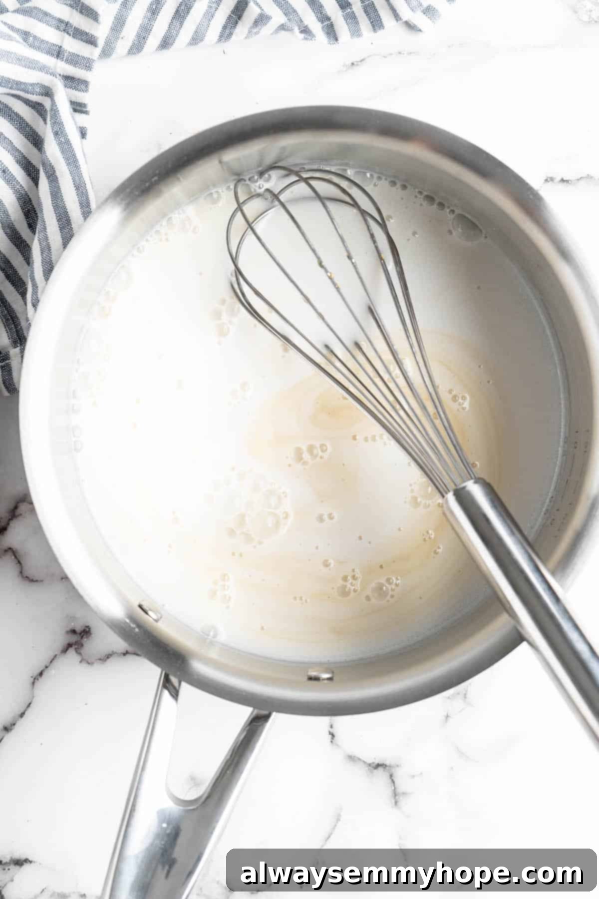 Overhead view of full-fat coconut milk and maple syrup being whisked together in a small saucepan over medium heat, beginning the cooking process