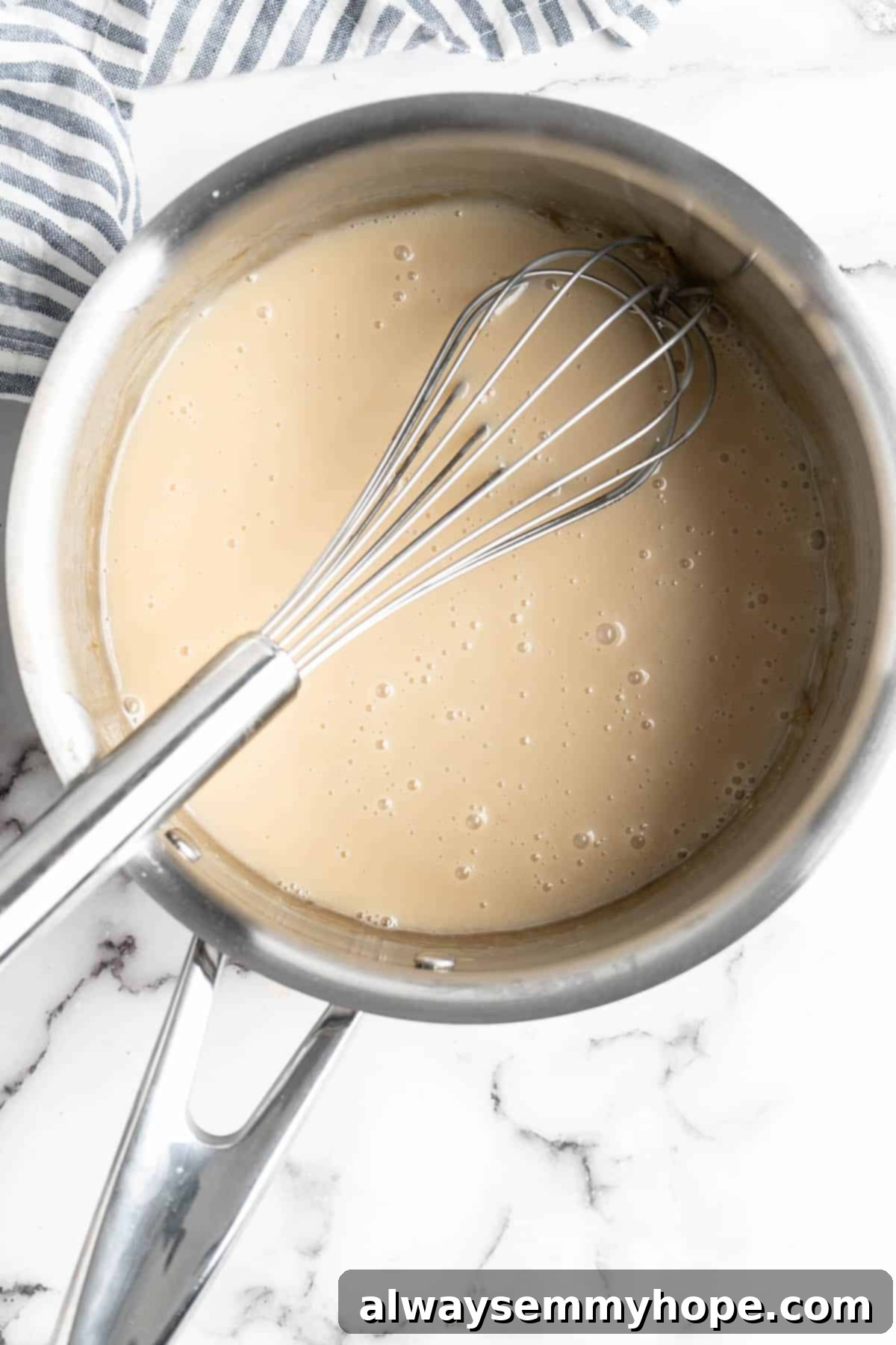Thick, reduced vegan condensed milk resting in a pan with a whisk, after simmering, ready to be transferred for storage