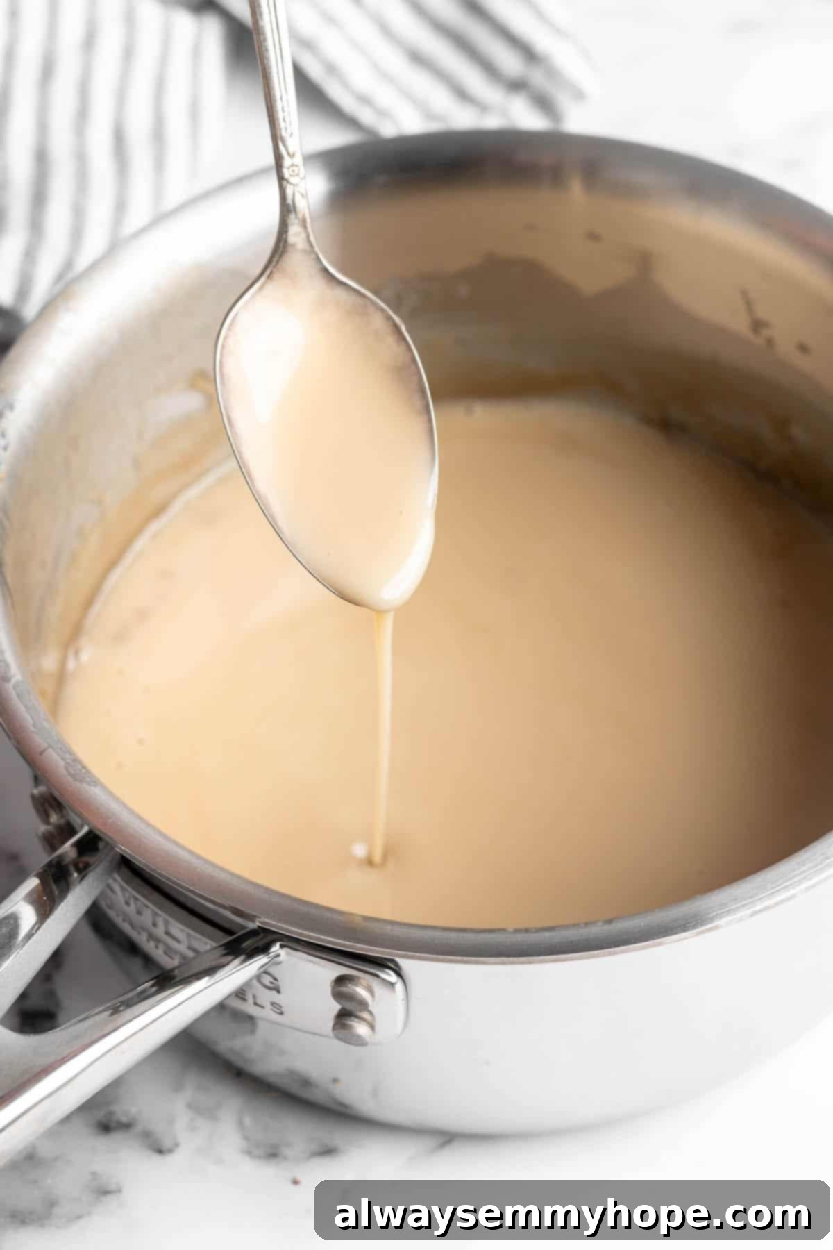 Spoon drizzling a generous amount of thick, golden vegan condensed milk into a saucepan, ready to be incorporated into another delicious recipe