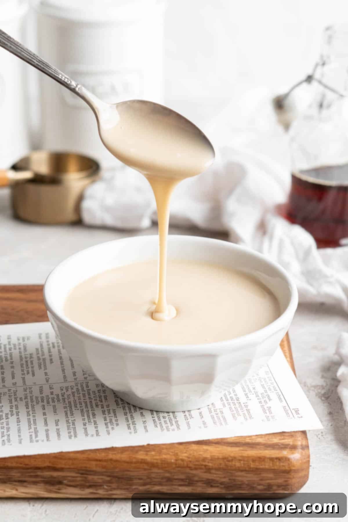 A spoon delicately drizzles creamy vegan condensed milk into a serving bowl, highlighting its perfect texture and readiness for use in various desserts