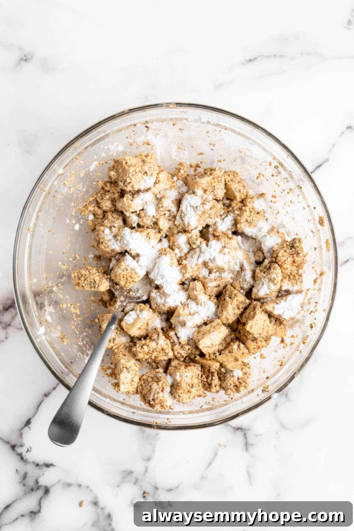 This Jamaican jerk tofu is the real deal! It's spicy, saucy, and just a little bit sweet. It's also super easy to make for a weeknight meal! Overhead view of tofu tossed with cornstarch in glass bowl