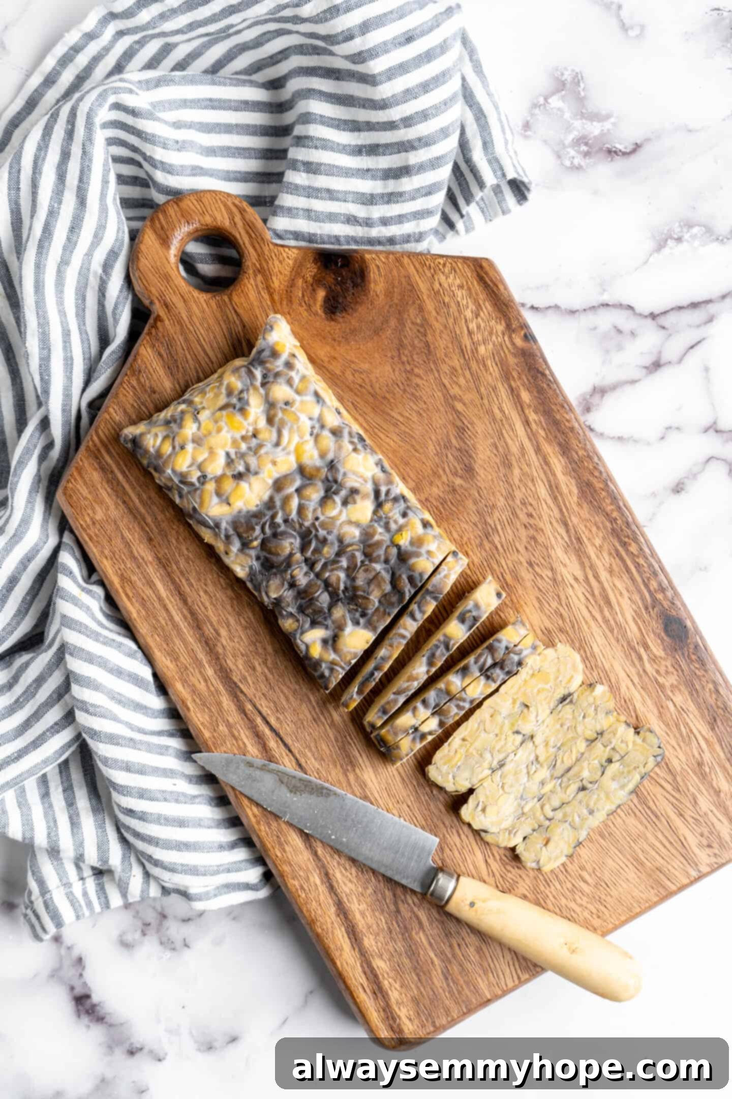 Close-up of a slab of steamed tempeh being thinly sliced on a cutting board, ready for marinade.