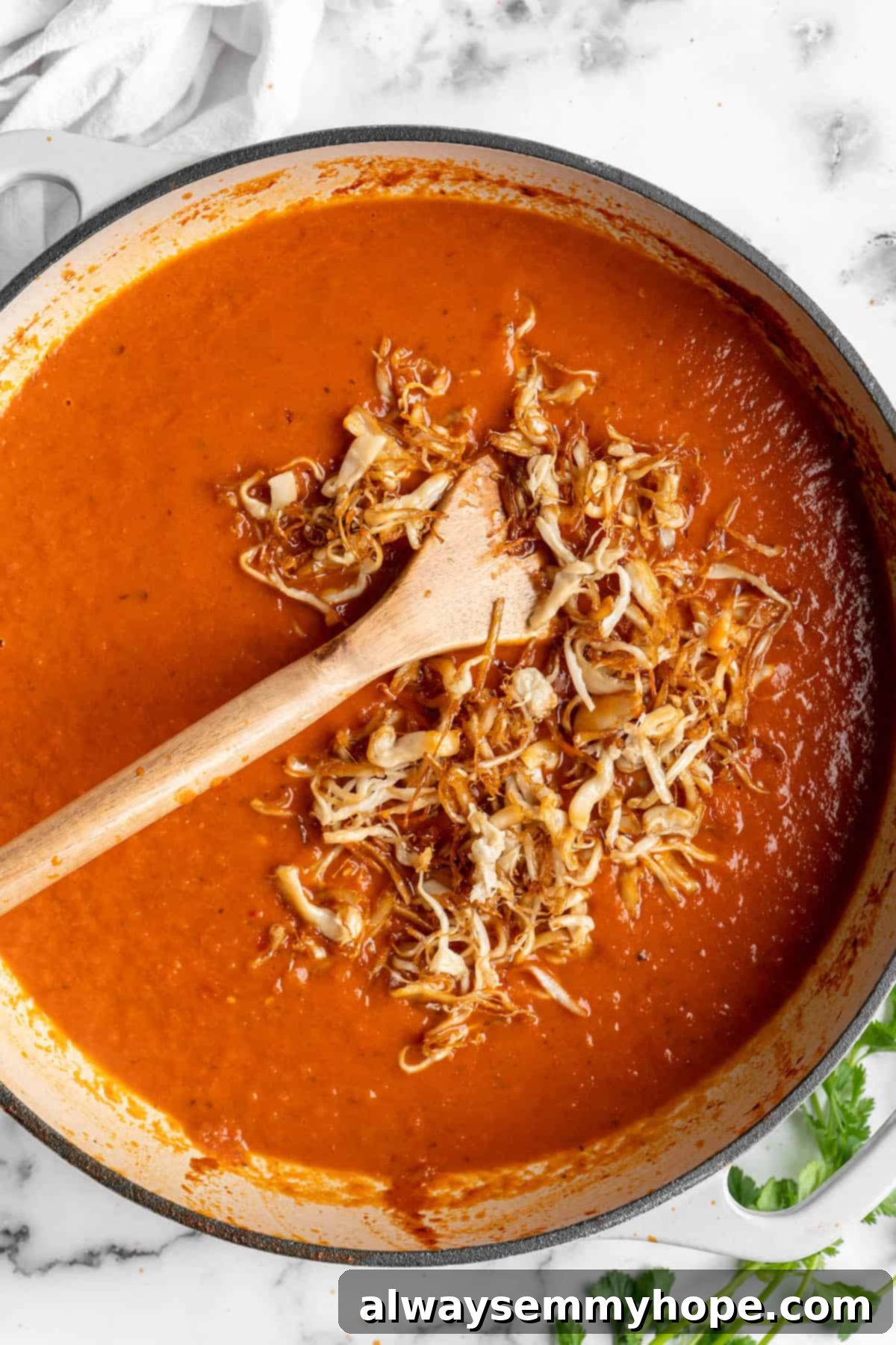 Vegan birria tacos use king oyster mushrooms to mimic the texture/flavour of the original. They’re smoky, crispy, and perfect for dipping! Overhead view of shredded mushrooms being stirred into birria sauce.