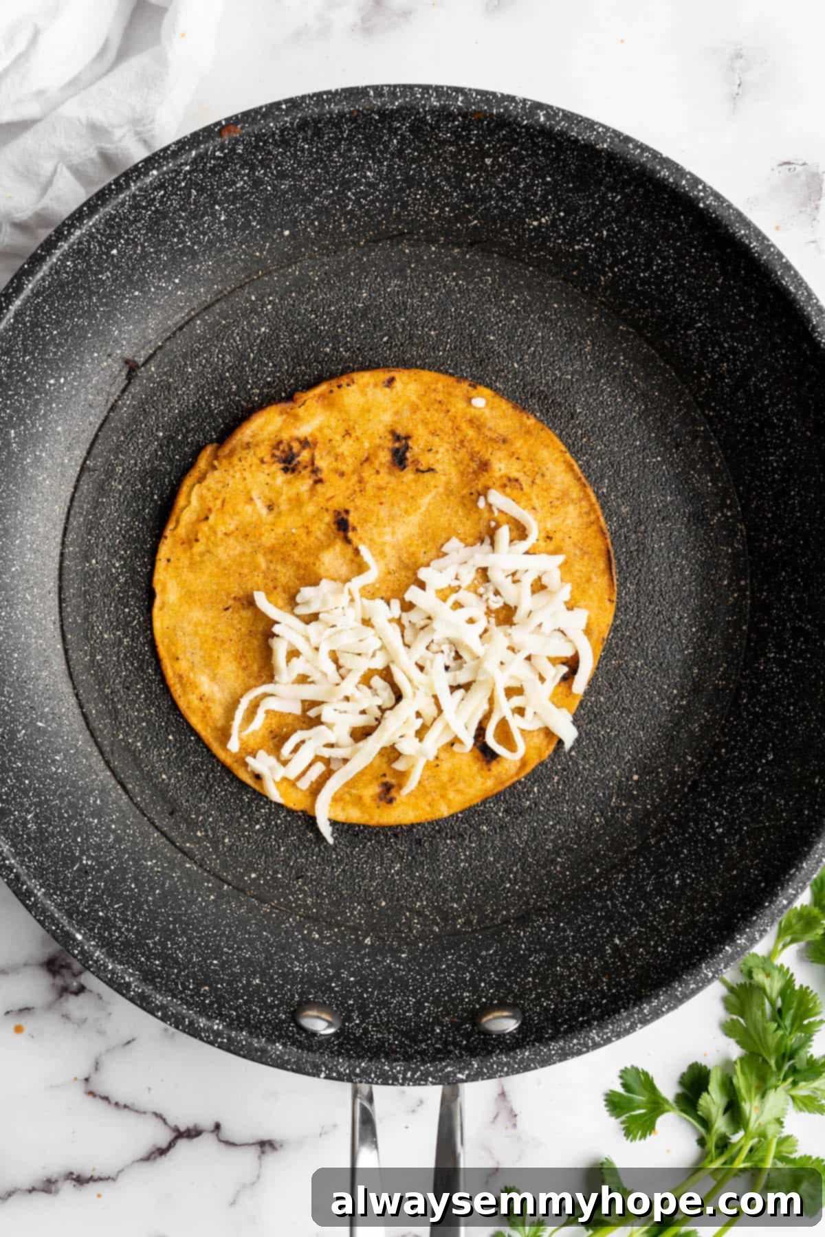 Vegan birria tacos use king oyster mushrooms to mimic the texture/flavour of the original. They’re smoky, crispy, and perfect for dipping! Overhead view of a tortilla in a skillet, topped with vegan cheese.