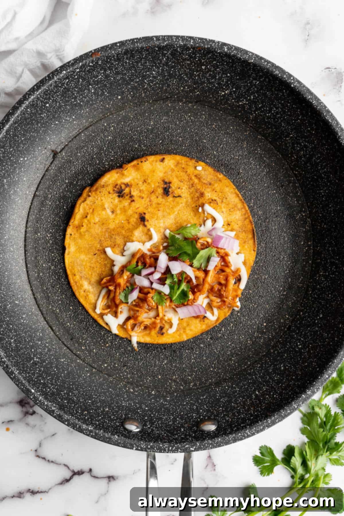 Vegan birria tacos use king oyster mushrooms to mimic the texture/flavour of the original. They’re smoky, crispy, and perfect for dipping! Overhead view of a tortilla in a skillet topped with taco fillings.