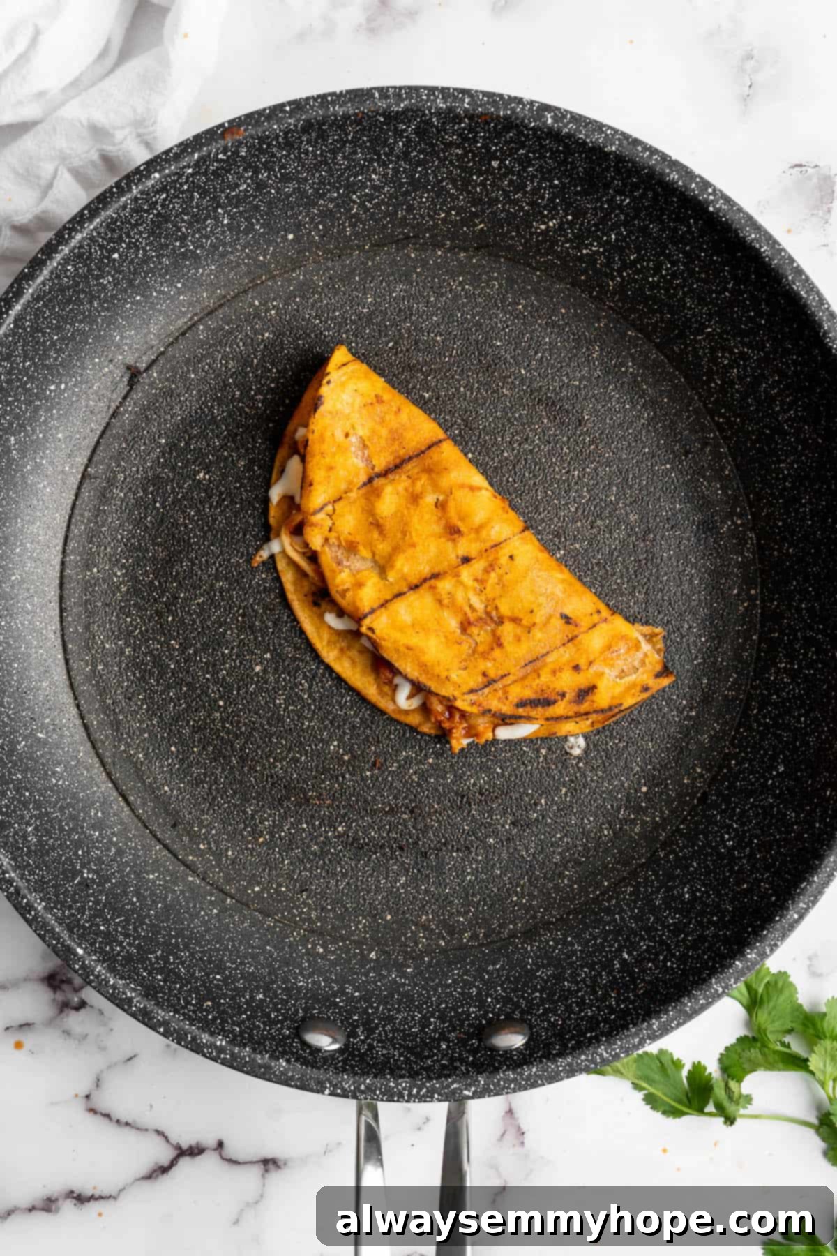 Vegan birria tacos use king oyster mushrooms to mimic the texture/flavour of the original. They’re smoky, crispy, and perfect for dipping! Overhead view of a vegan birria taco in a skillet.