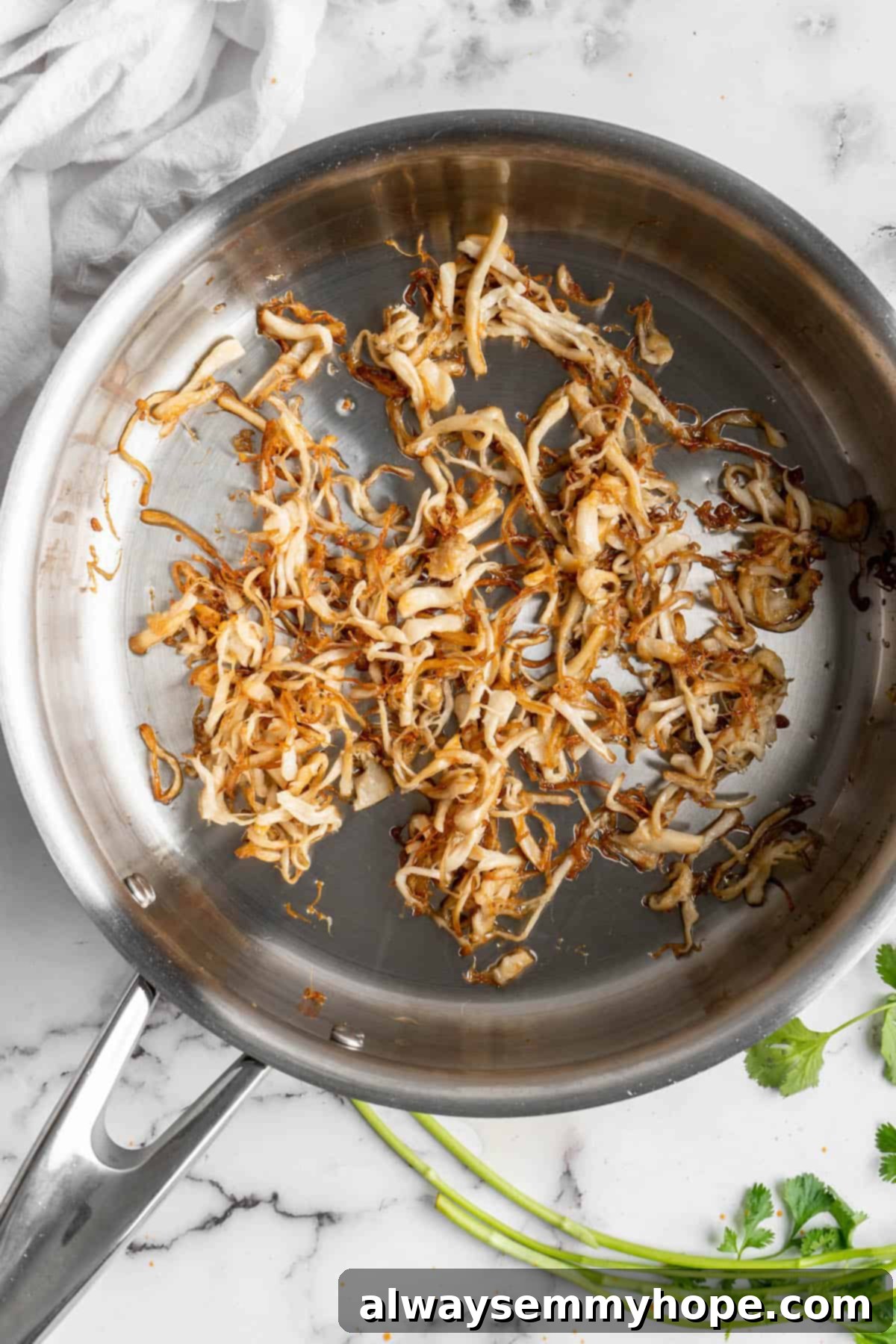 Vegan birria tacos use king oyster mushrooms to mimic the texture/flavour of the original. They’re smoky, crispy, and perfect for dipping! Overhead view of shredded oyster mushrooms in a skillet.