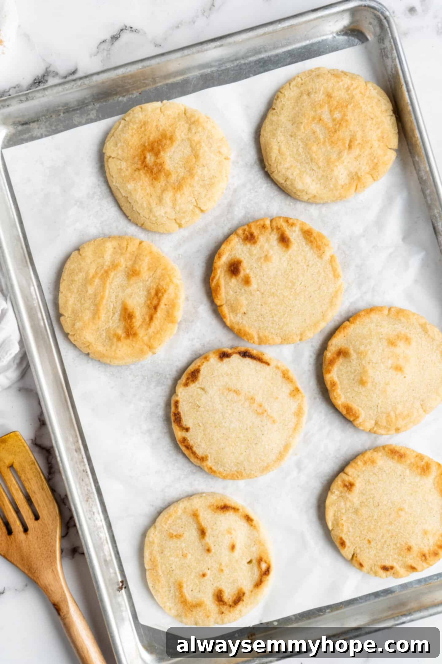 This step-by-step tutorial will show you how to make perfect vegan arepas with just a few ingredients. They're easier to make than you think! Overhead shot of pan-fried vegan arepas neatly arranged on a parchment-lined baking sheet, ready for their final bake in the oven.