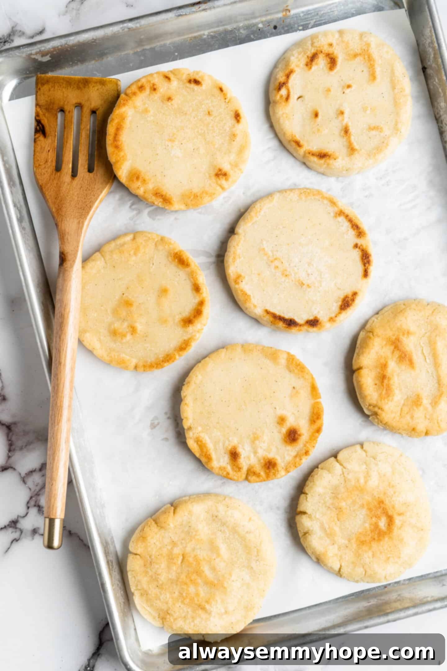 This step-by-step tutorial will show you how to make perfect vegan arepas with just a few ingredients. They're easier to make than you think! Overhead view of several golden-brown vegan arepas cooling on a parchment-lined baking sheet after being baked to perfection.
