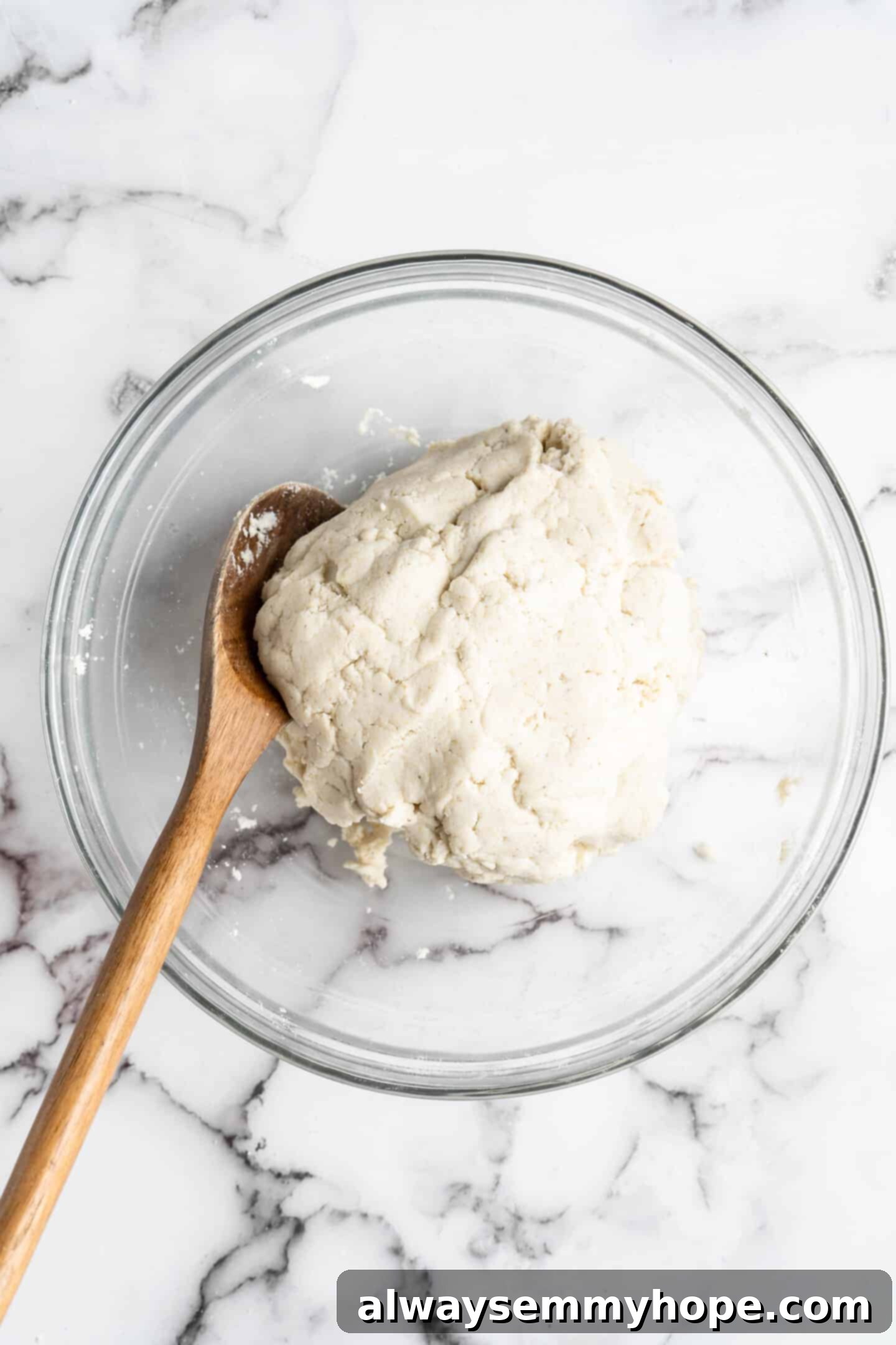 This step-by-step tutorial will show you how to make perfect vegan arepas with just a few ingredients. They're easier to make than you think! A bowl of freshly prepared vegan arepa dough, with a wooden spoon resting beside it, indicating readiness for shaping.