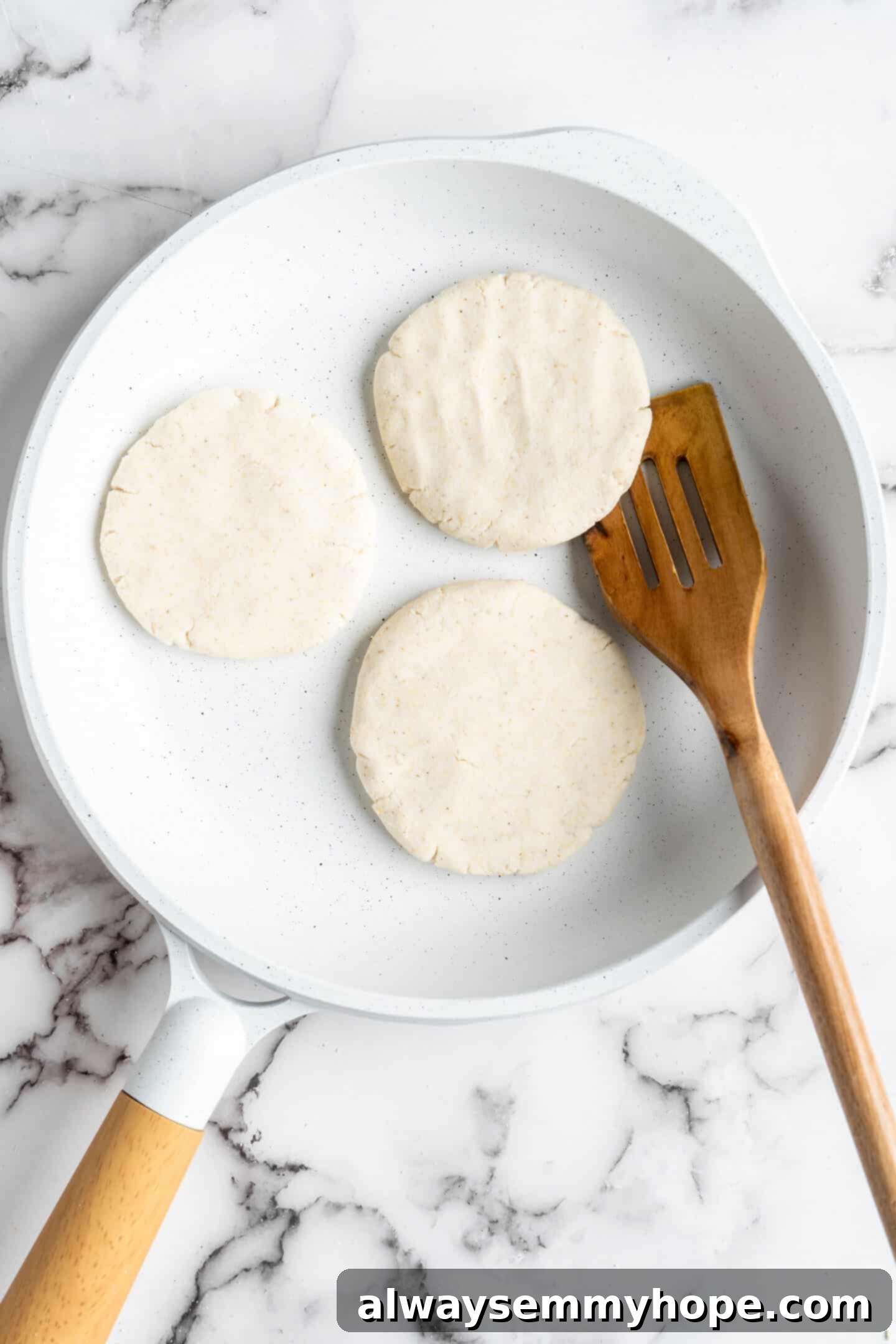 This step-by-step tutorial will show you how to make perfect vegan arepas with just a few ingredients. They're easier to make than you think! Overhead view of three uncooked vegan arepas neatly arranged in a hot skillet, ready for pan-frying.