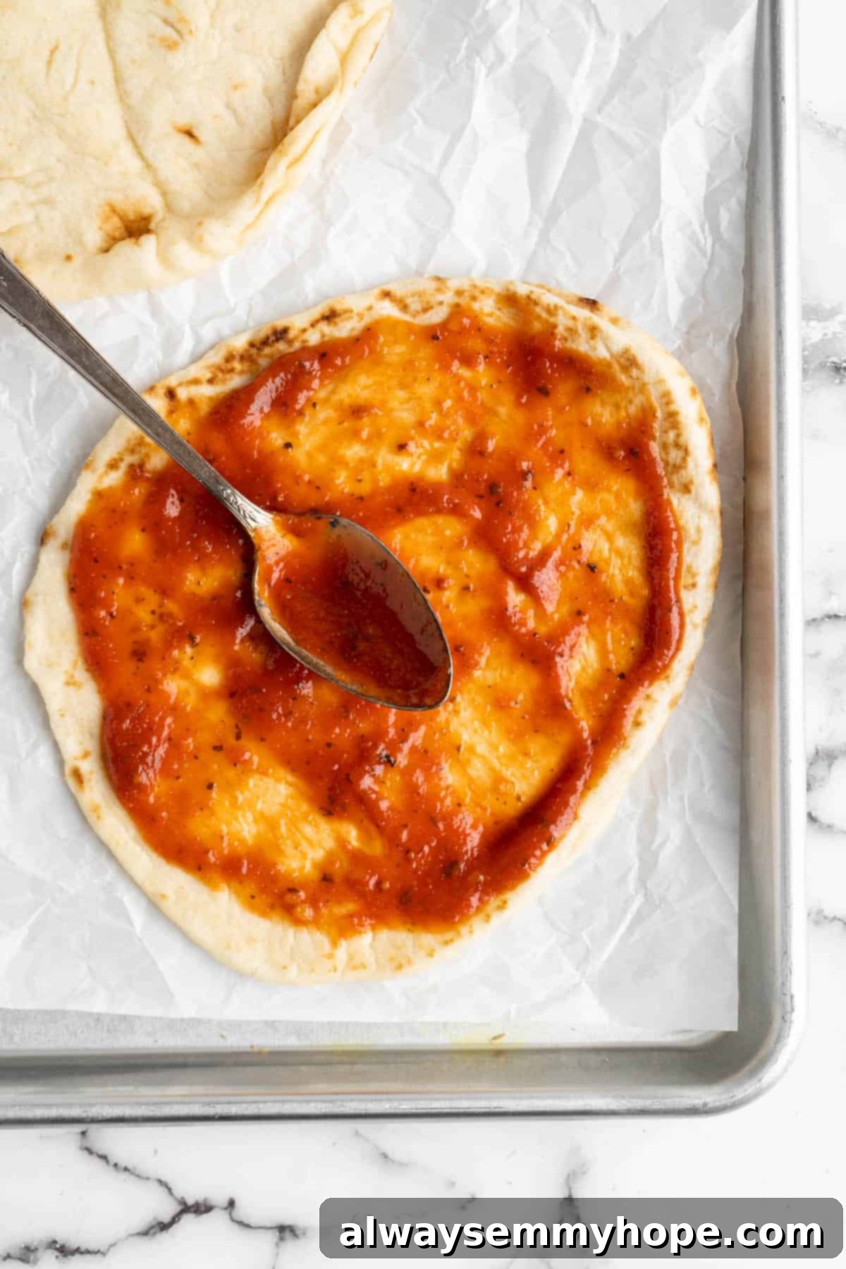 Close-up overhead view of pizza sauce being skillfully spread across a vegan naan, preparing it for toppings.