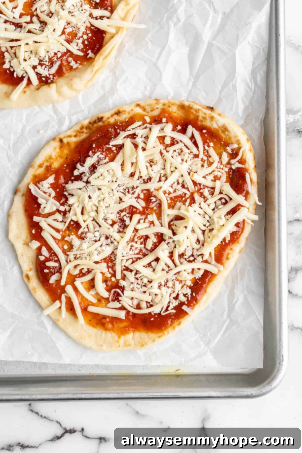 Overhead view of a vegan naan pizza base generously topped with vegan mozzarella cheese, ready for further toppings.