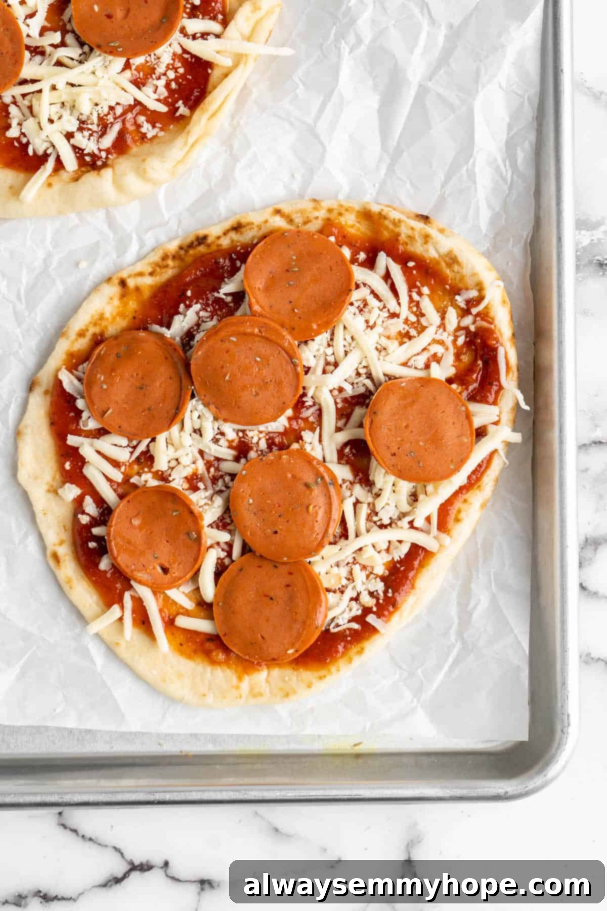 Overhead view of a vegan naan pizza topped with vegan pepperoni and vegetables, arranged on a sheet pan ready for baking.