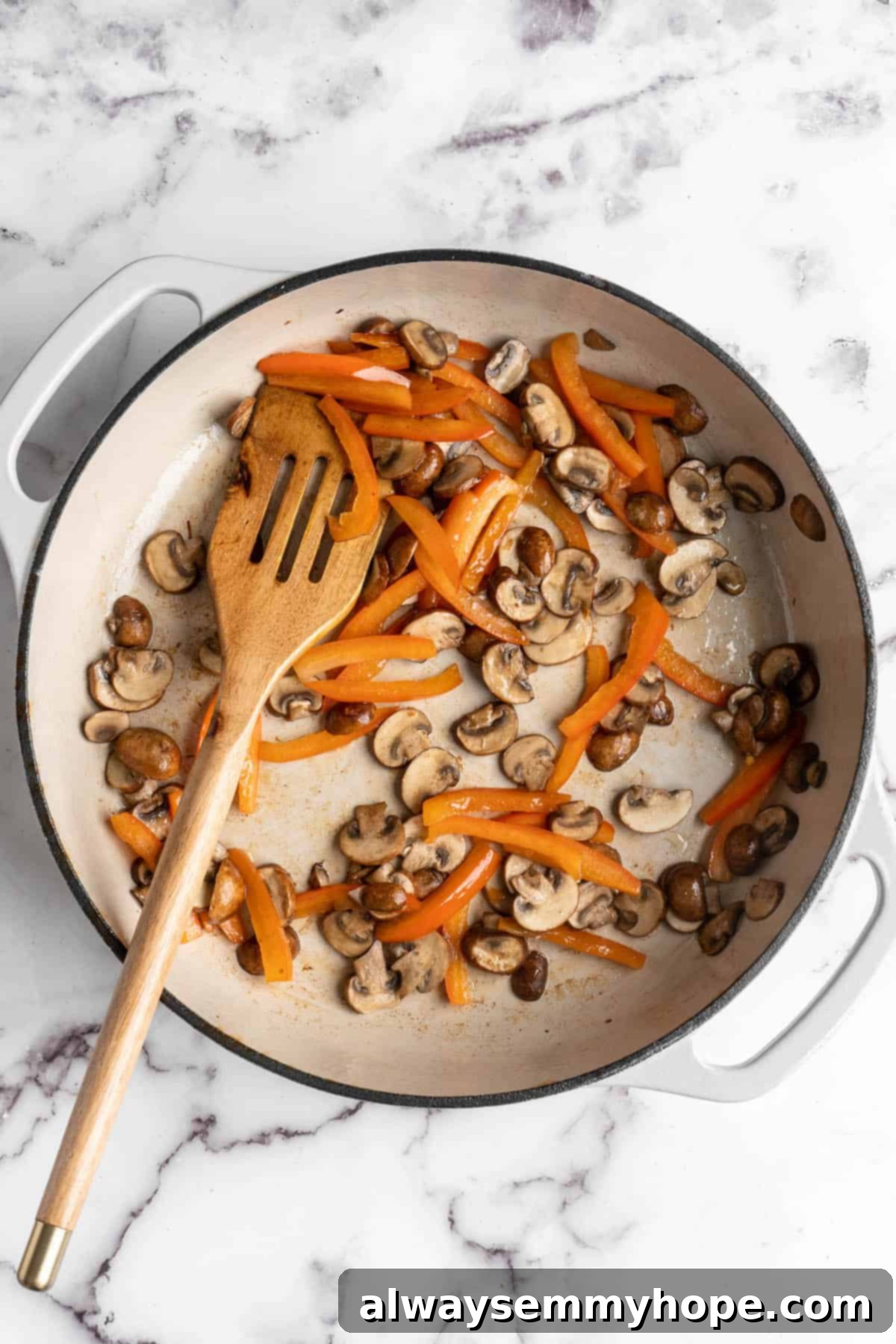 Overhead view of red bell pepper strips and mushrooms in skillet