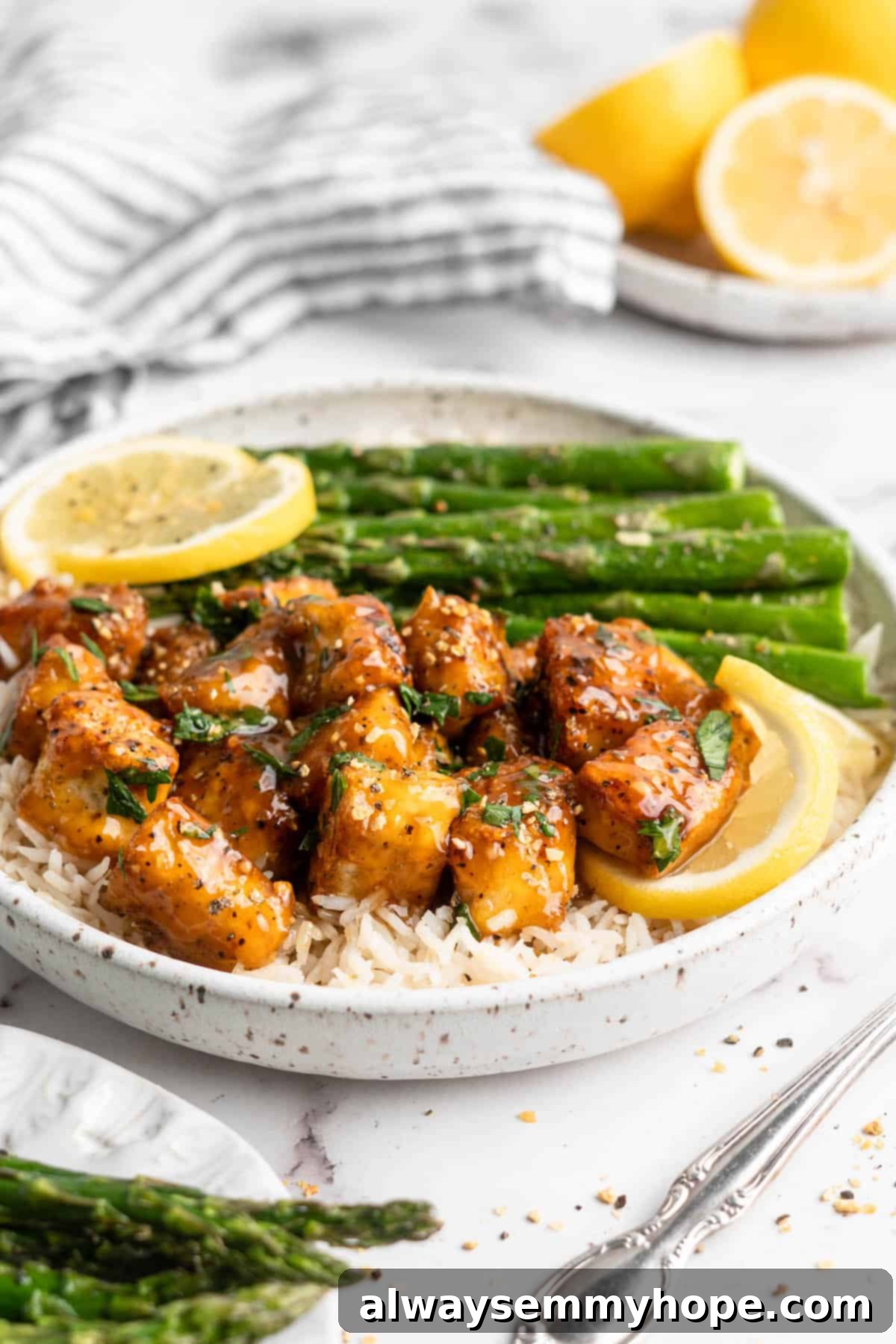 This lemon pepper tofu is crispy and saucy, with the perfect chewy texture. It takes minutes to make and it's absolutely packed with flavour! Plate of lemon pepper tofu with rice and asparagus.