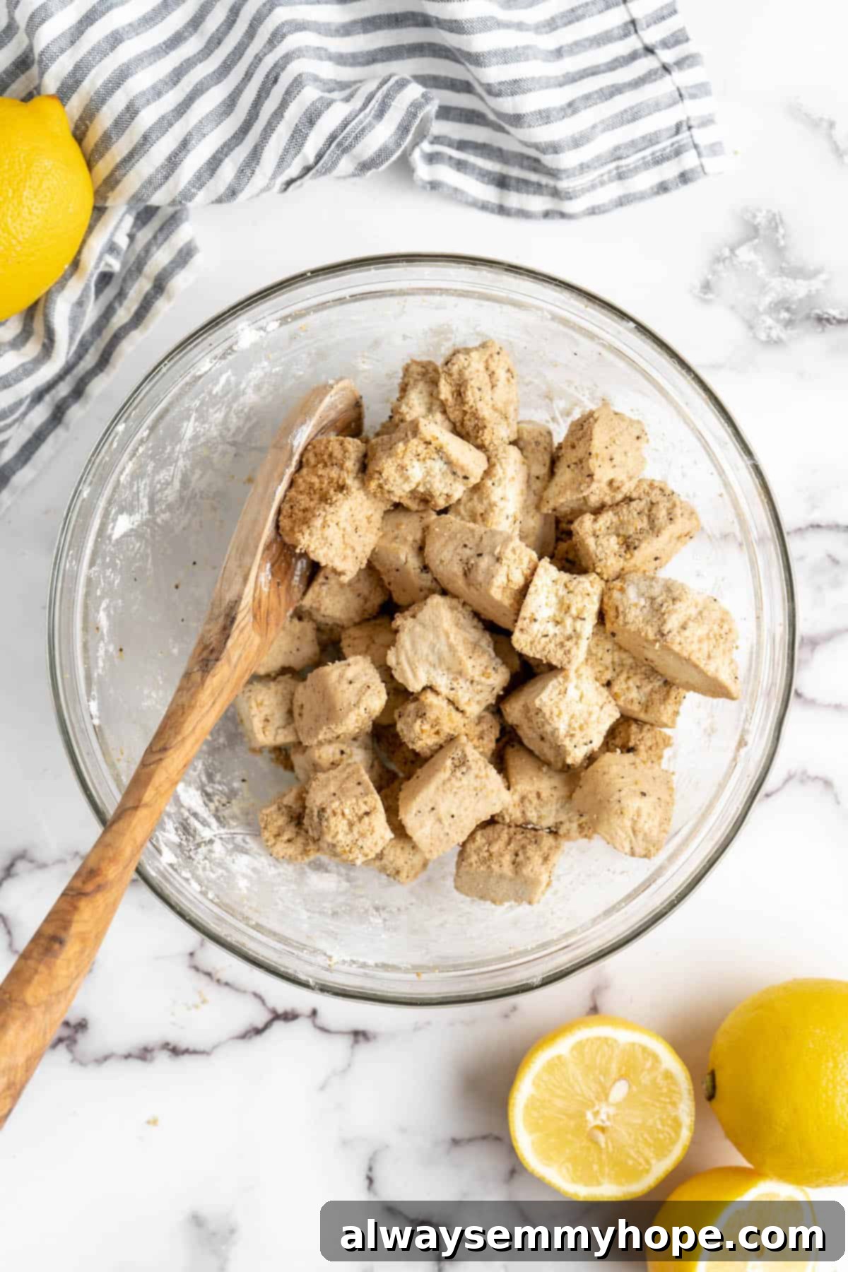 This lemon pepper tofu is crispy and saucy, with the perfect chewy texture. It takes minutes to make and it's absolutely packed with flavour! Overhead view of tofu in a glass bowl with cornstarch and seasonings.