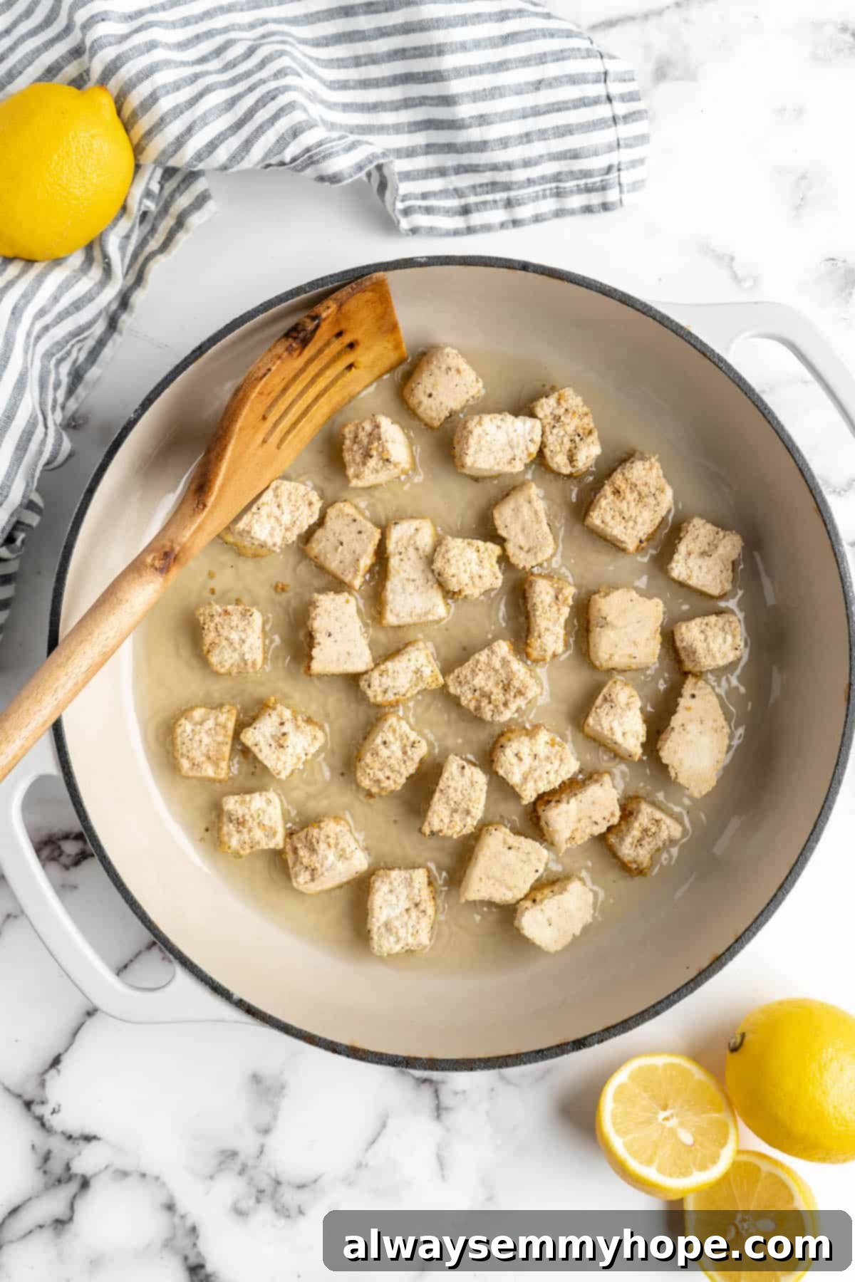 This lemon pepper tofu is crispy and saucy, with the perfect chewy texture. It takes minutes to make and it's absolutely packed with flavour! Overhead view of tofu and oil in a skillet.