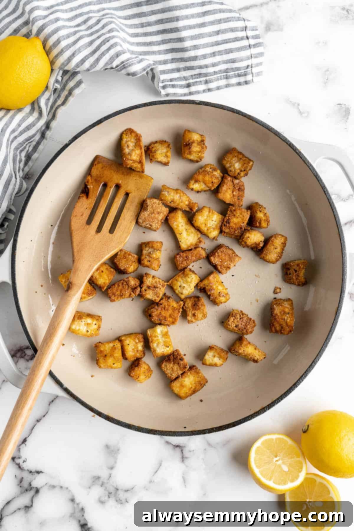 This lemon pepper tofu is crispy and saucy, with the perfect chewy texture. It takes minutes to make and it's absolutely packed with flavour! Overhead view of tofu in a skillet with a wooden spatula.