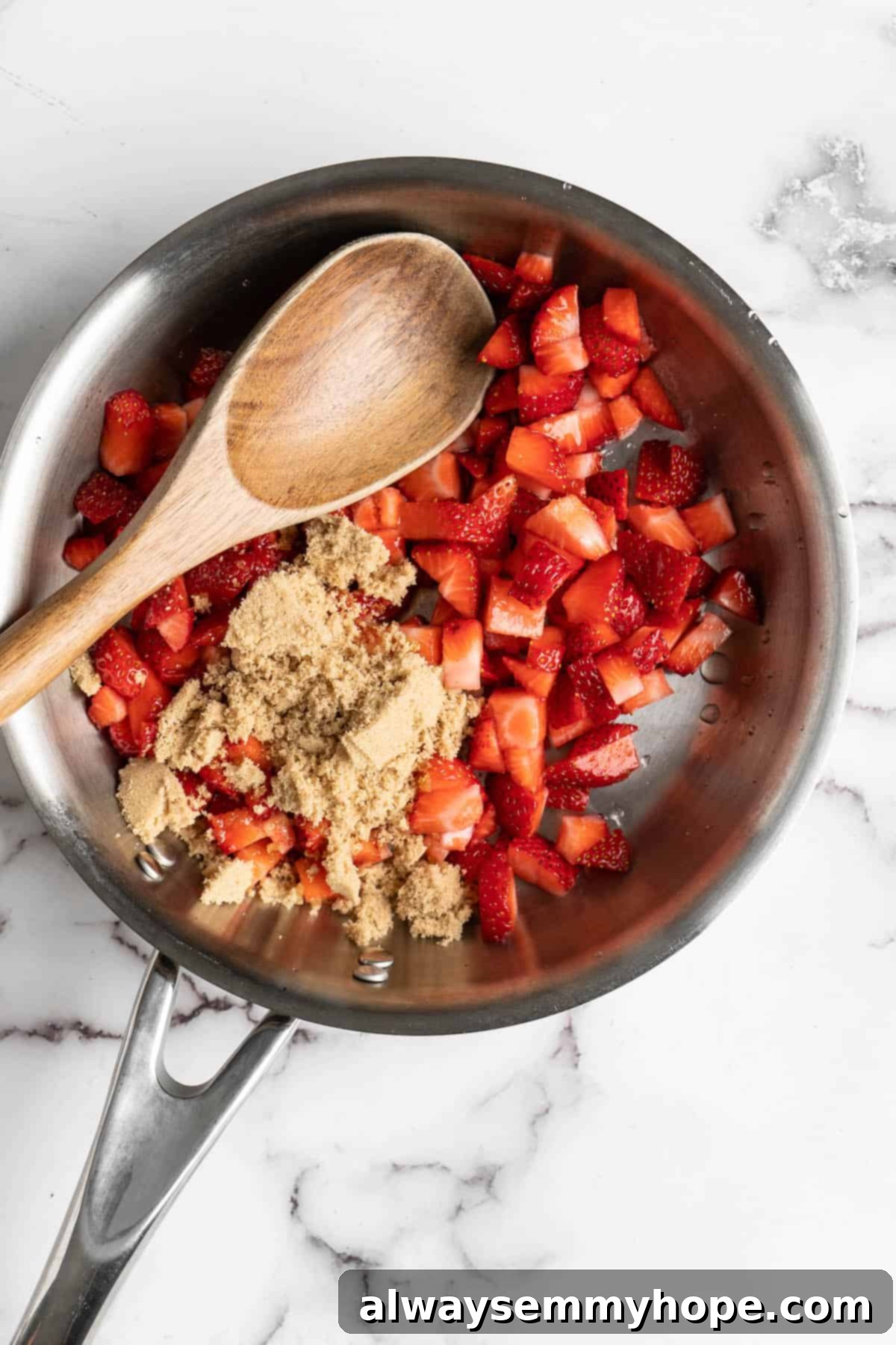 How to make vegan Korean strawberry milk! This easy recipe is made with 4 simple ingredients and each glass is full of fresh strawberries. Overhead view of a saucepan containing diced strawberries and brown sugar, ready to be cooked into a syrup.