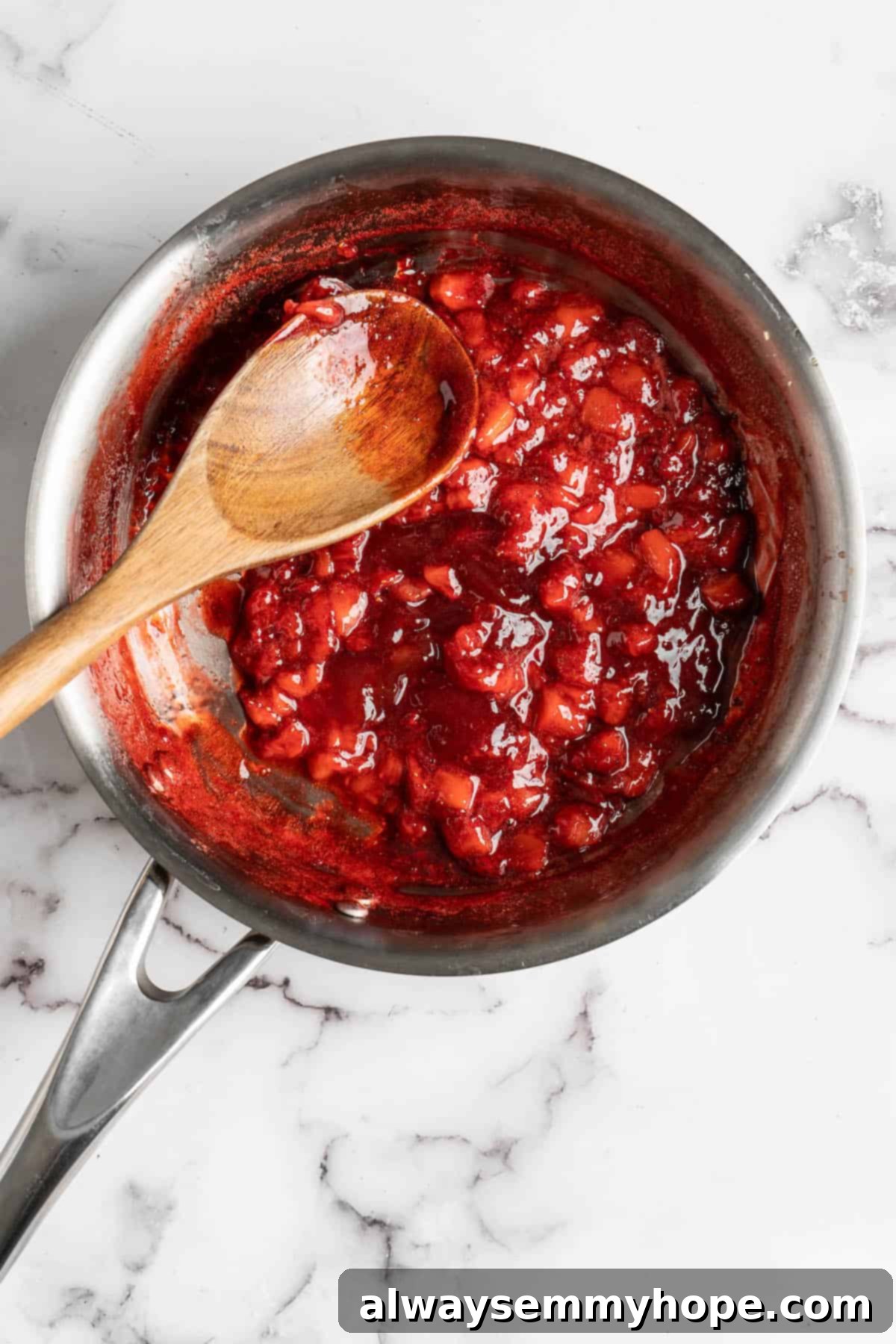 How to make vegan Korean strawberry milk! This easy recipe is made with 4 simple ingredients and each glass is full of fresh strawberries. Overhead view of a cooked strawberry syrup in a saucepan, showing a thickened, jam-like consistency with some berry pieces.