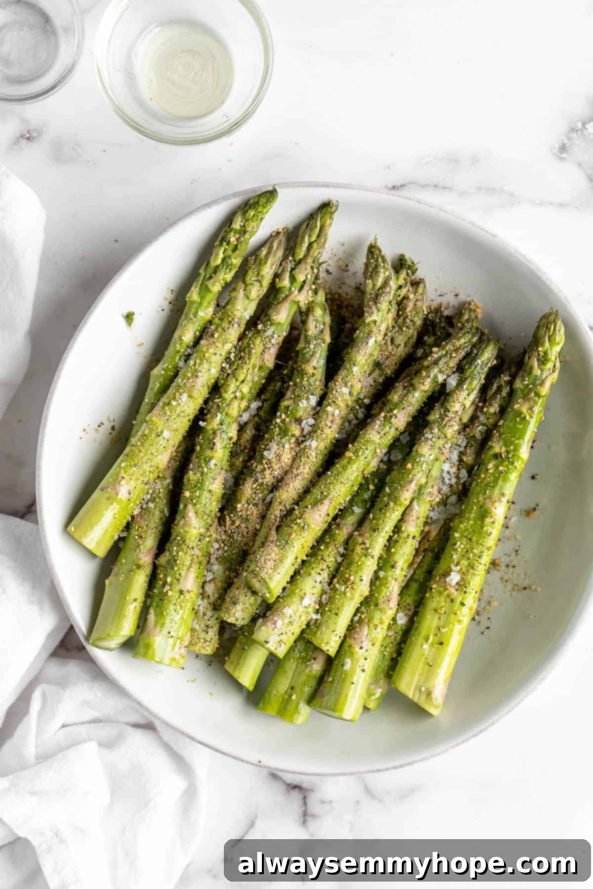 This easy lemon pepper air fryer asparagus is the perfect side dish for busy weeknights. It's done in just 10 minutes from start to finish! Overhead view of asparagus in a bowl, evenly coated with lemon pepper seasoning, garlic powder, and sea salt.