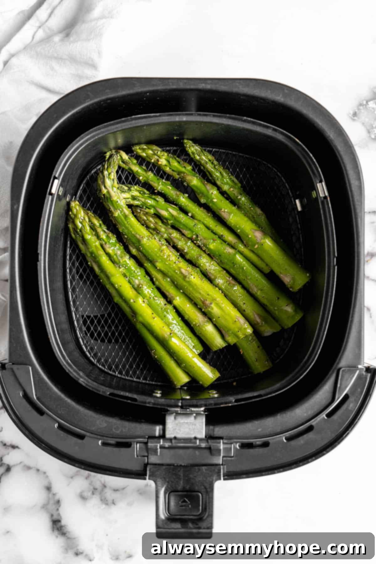 This easy lemon pepper air fryer asparagus is the perfect side dish for busy weeknights. It's done in just 10 minutes from start to finish! Overhead view of seasoned asparagus spears arranged in a single layer in the air fryer basket, ready for cooking.