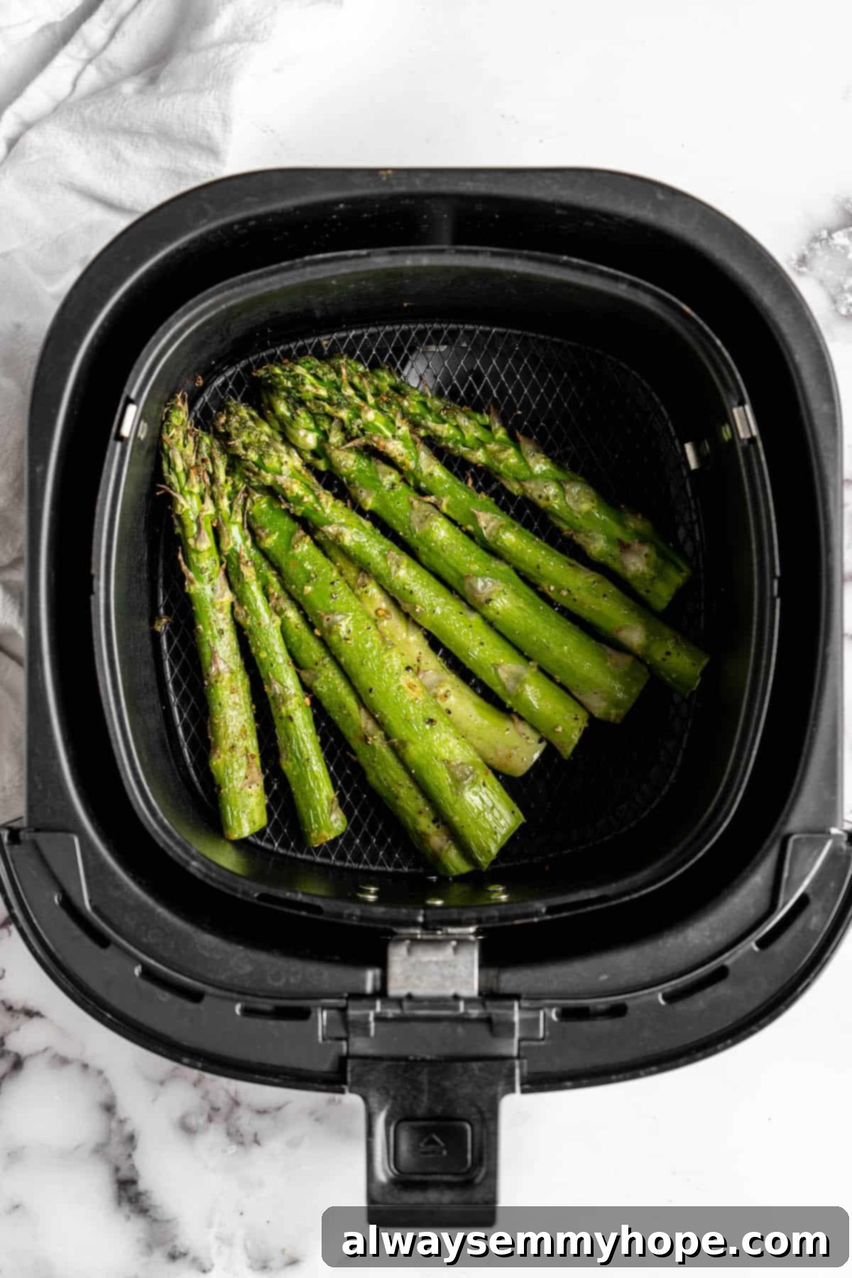This easy lemon pepper air fryer asparagus is the perfect side dish for busy weeknights. It's done in just 10 minutes from start to finish! Overhead view of the air fryer basket filled with beautifully cooked asparagus, showing crispy tips and tender green stalks.