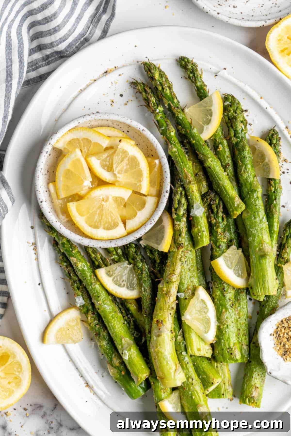 This easy lemon pepper air fryer asparagus is the perfect side dish for busy weeknights. It's done in just 10 minutes from start to finish! Overhead view of a beautiful serving platter piled high with perfectly cooked lemon pepper air fryer asparagus, accompanied by a bowl of fresh lemon wedges for garnish.