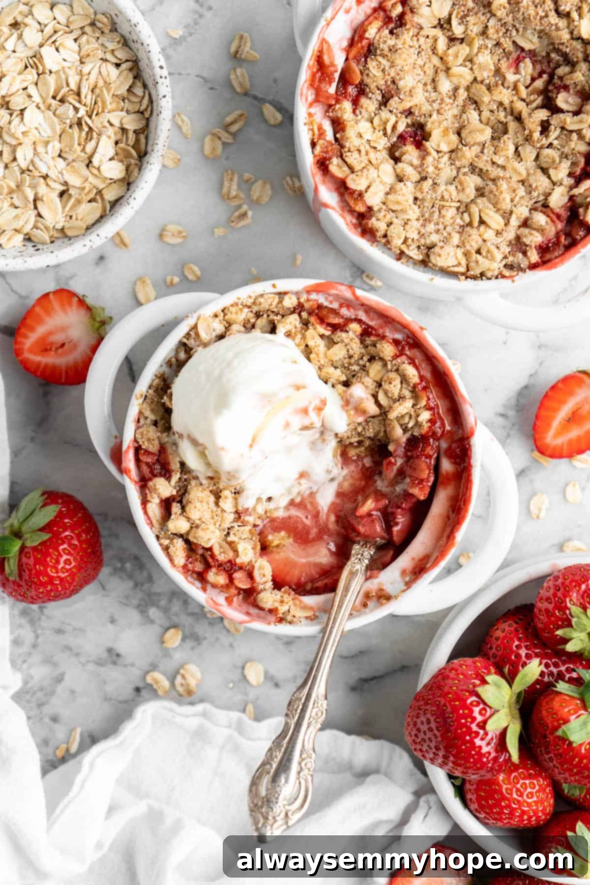 This vegan strawberry crumble is easy as can be! You only need 5 ingredients and a few minutes of assembly for the perfect summer dessert. Overhead view of strawberry crumble in ramekins, with one topped with vanilla ice cream