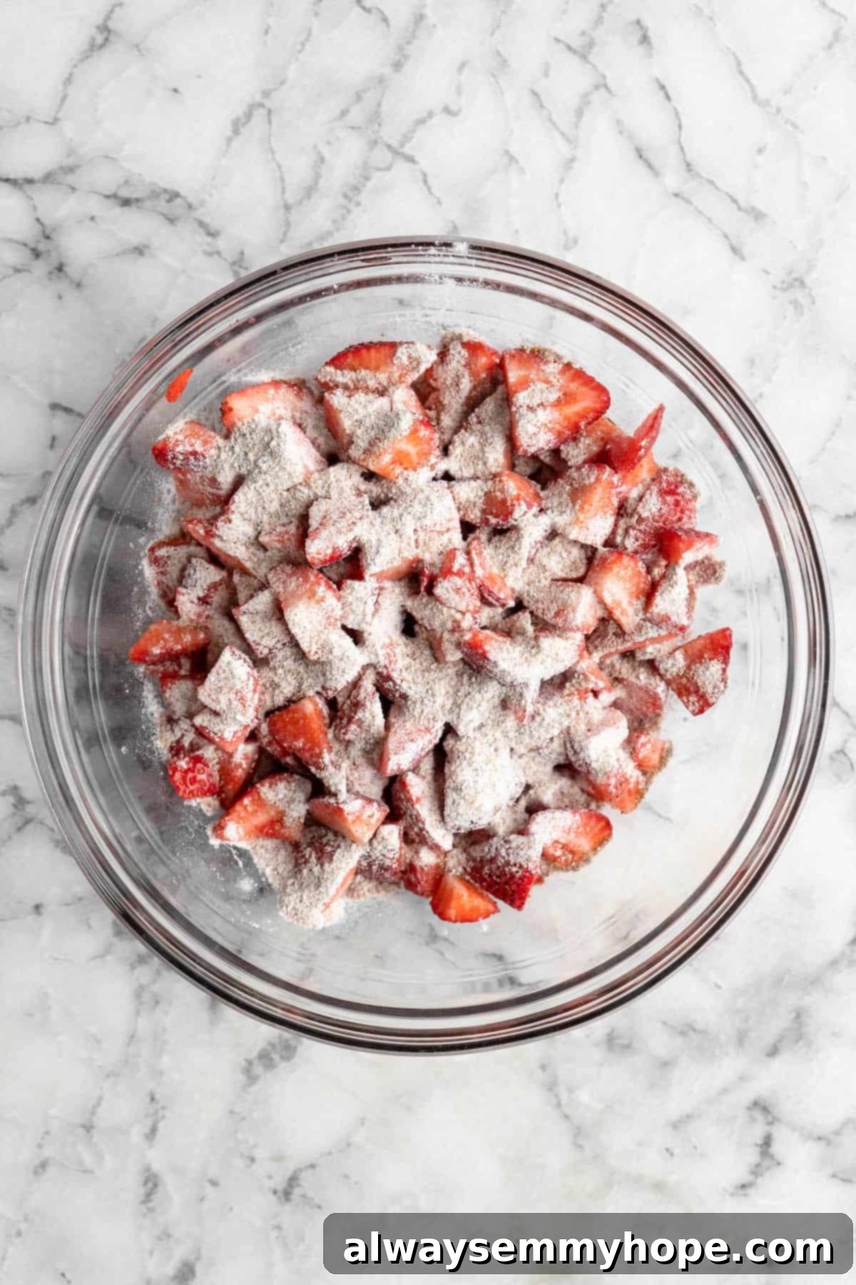 This vegan strawberry crumble is easy as can be! You only need 5 ingredients and a few minutes of assembly for the perfect summer dessert. Overhead view of flour mixture sprinkled over strawberries in bowl