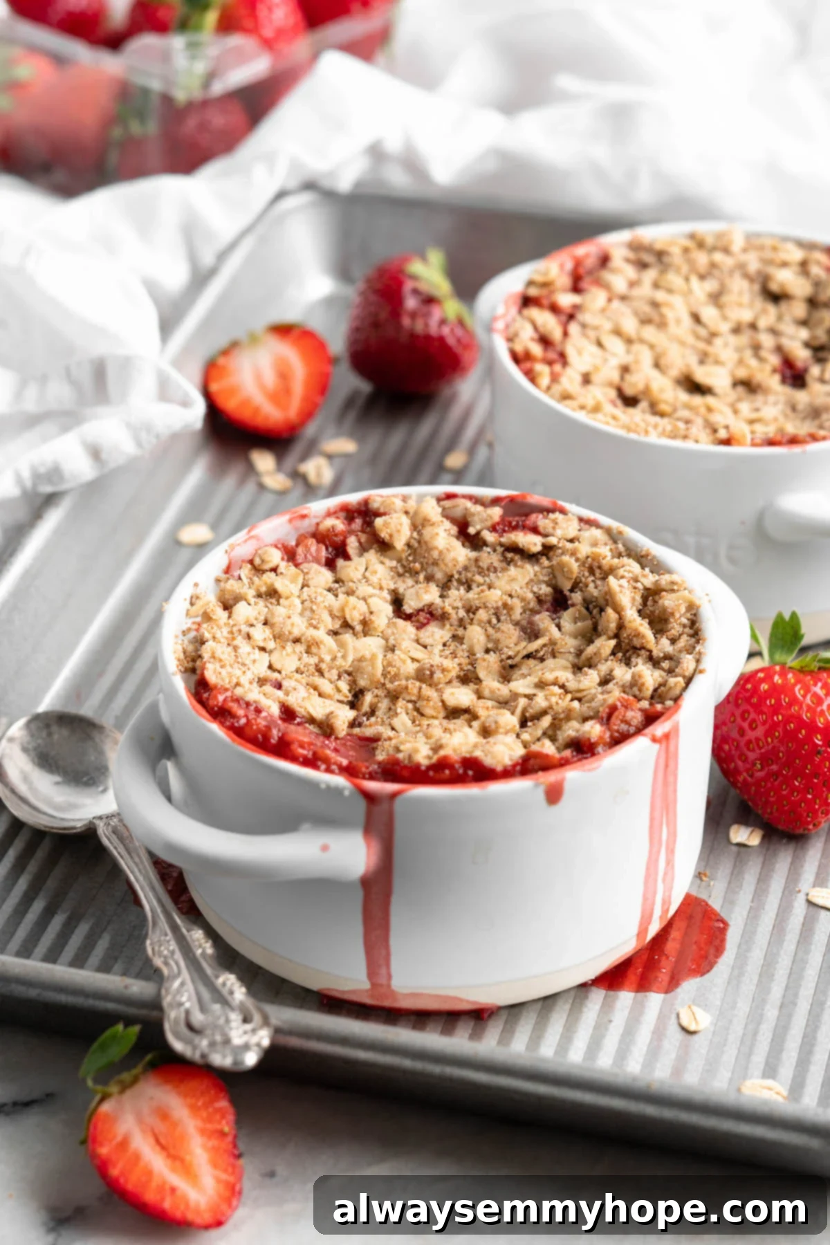This vegan strawberry crumble is easy as can be! You only need 5 ingredients and a few minutes of assembly for the perfect summer dessert. Two strawberry crumbles in ramekins on sheet pan